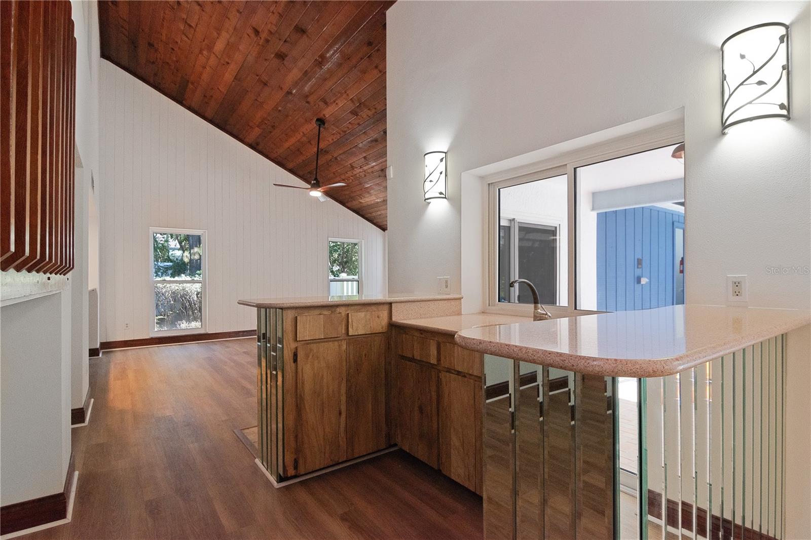 Wet Bar with Quartz Countertops, Sink and Storage Cabinets and Drawers connects Living and Family Room under Vaulted Ceilings with New Sconce Lighting, New Lighted Ceiling Fan, New Paint, New Vinyl Flooring and Hurricane-Rated Windows