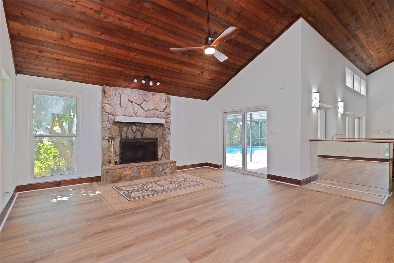 Family Room with Wood-Burning Fireplace featuring New Lighted Ceiling Fan, New Paint, New Vinyl Floors, Hurricane-Rated Windows and Hurricane-Rated Slider leading to Pool