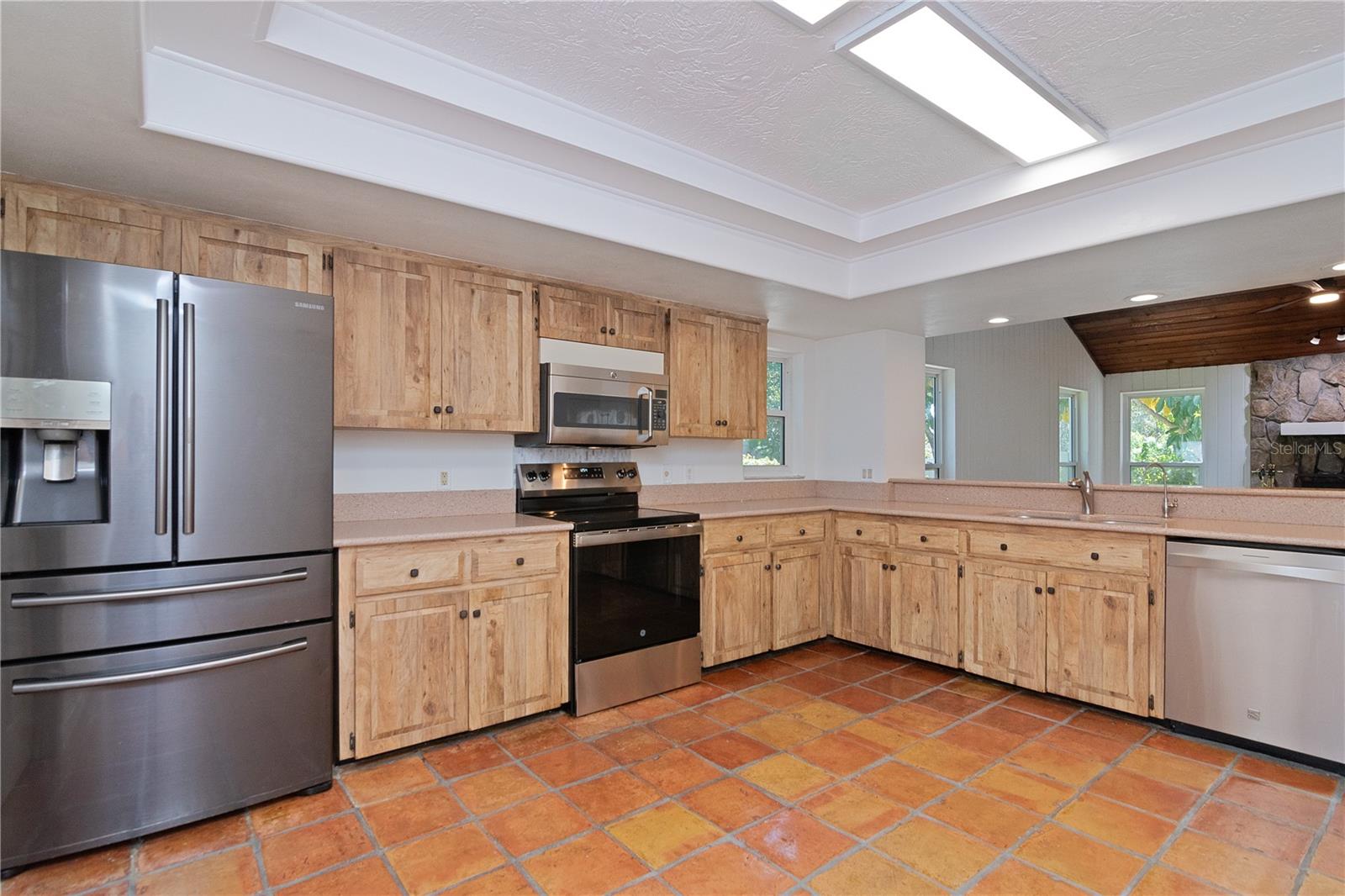 Remodeled Kitchen looking out to Family Room featuring New Oven/Range, New Paint, Newer Refrigerator, Newer Dishwasher, Quartz Countertops, Hurricane-Rated Window and Tile Floor