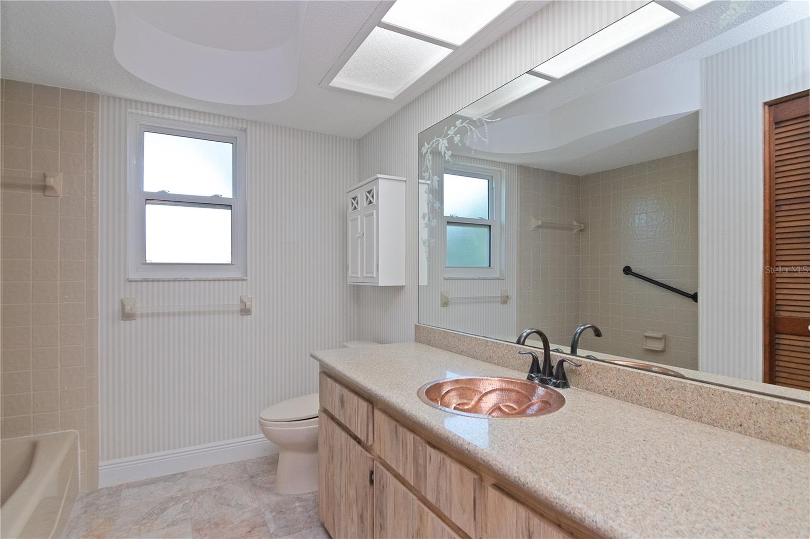 Upstairs Bathroom features New Paint, Hurricane-Rated Window, Copper Sink, Quartz Countertop and Tile Floor.