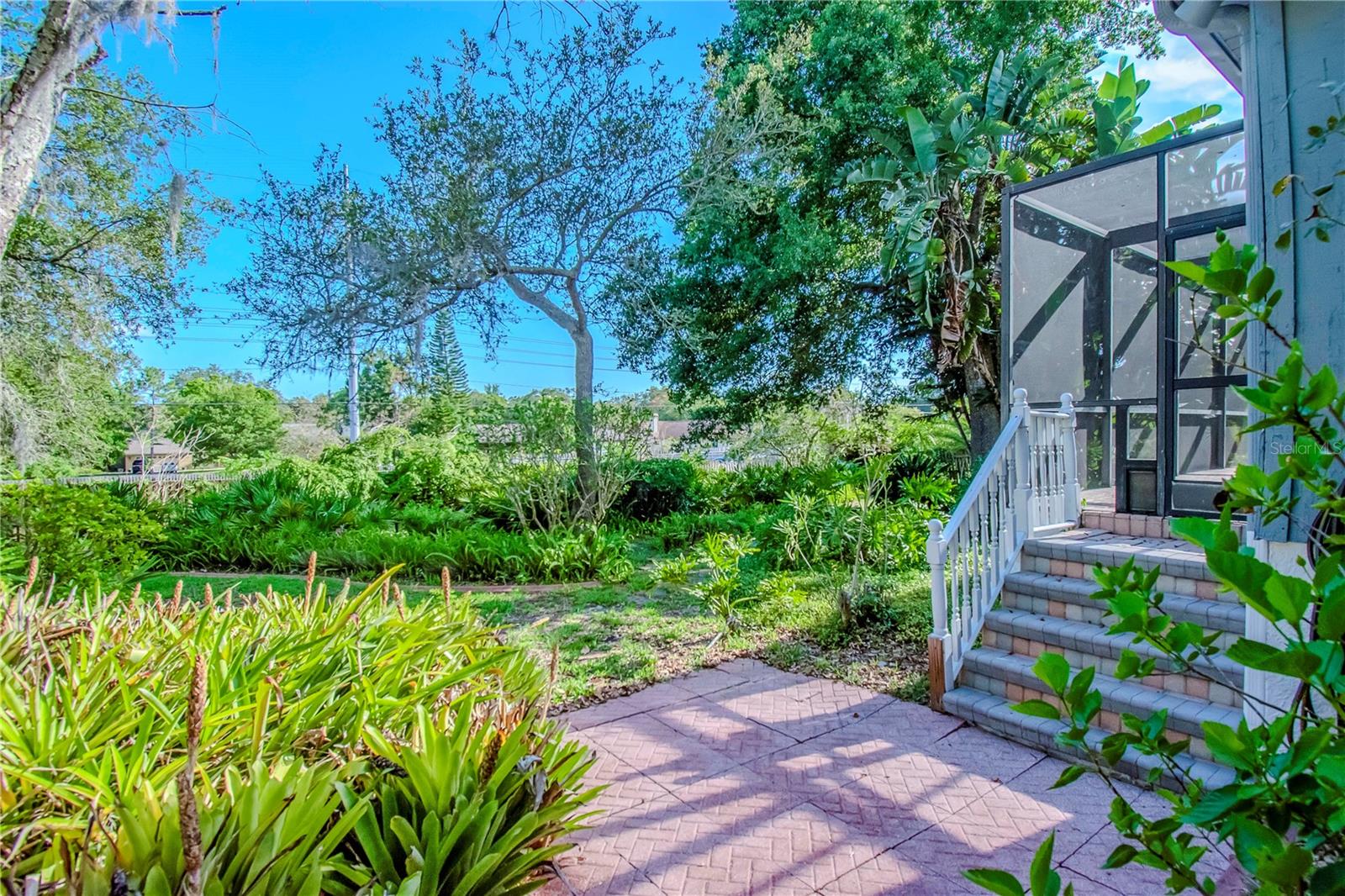 Stairs to Elevated Screened Lanai with Pavers and Lush Mature Landscaping