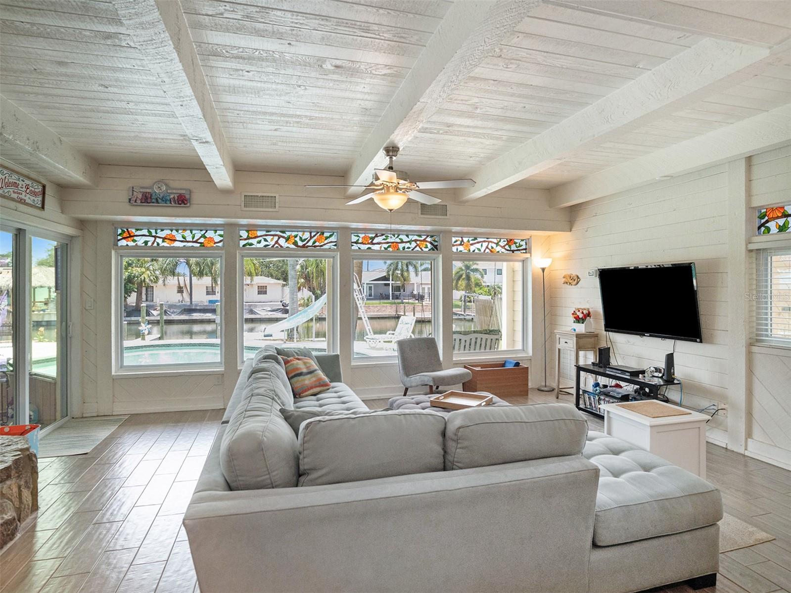 Family room with beamed ceiling, fireplace, and tons of natural light showcasing the pool and canal.