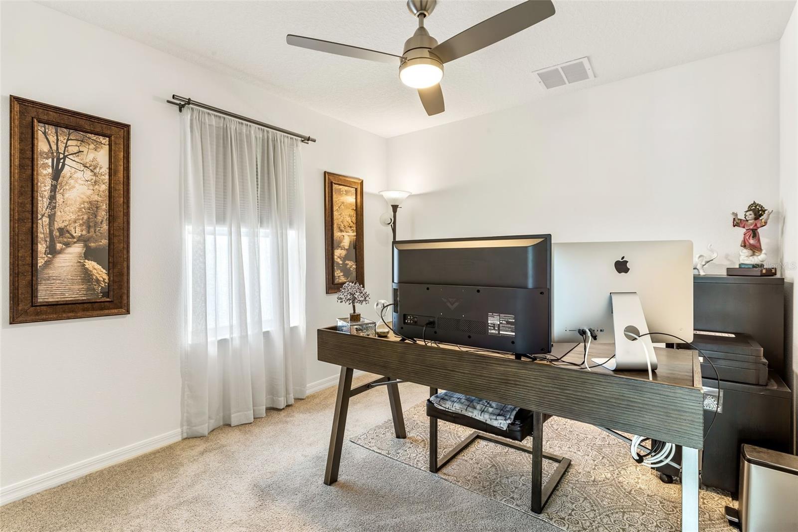 Bedroom 3 is being used as an office with overhead lighting fixture and window treatments.