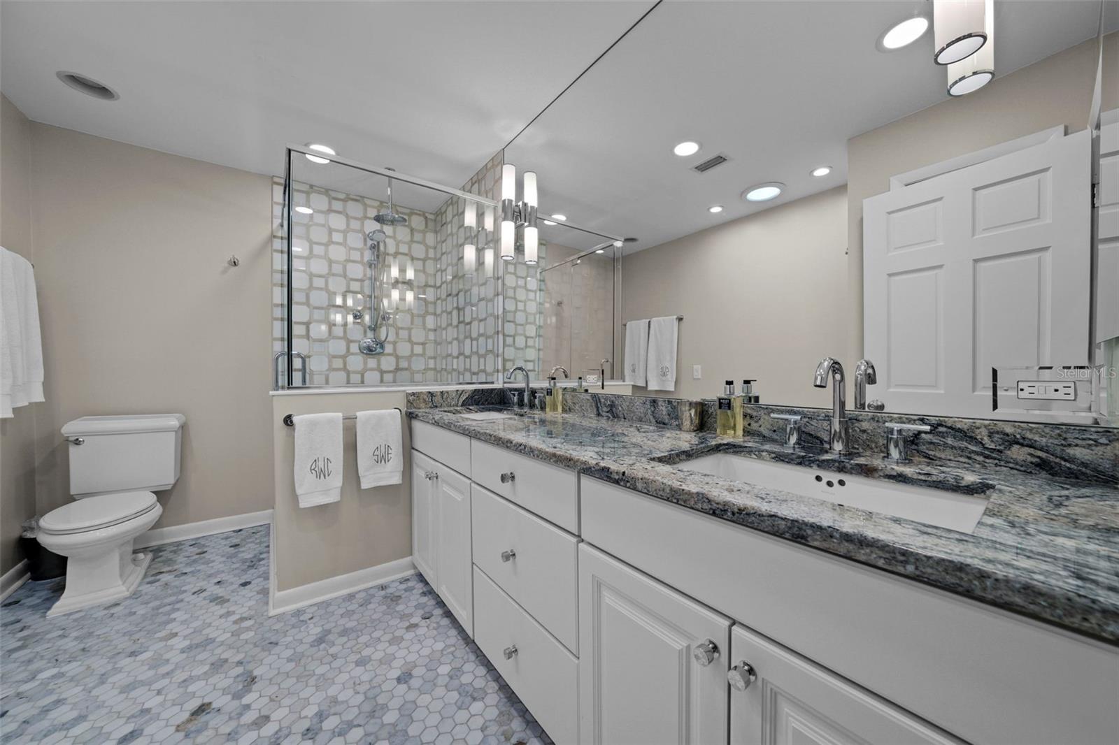 Primary bathroom features marble tiled floors and shower and dual sink vanity