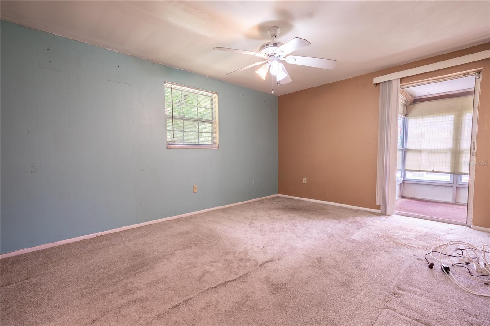 The primary bedroom features neutral tone carpet, a ceiling fan and sling glass doors to the Florida Room.