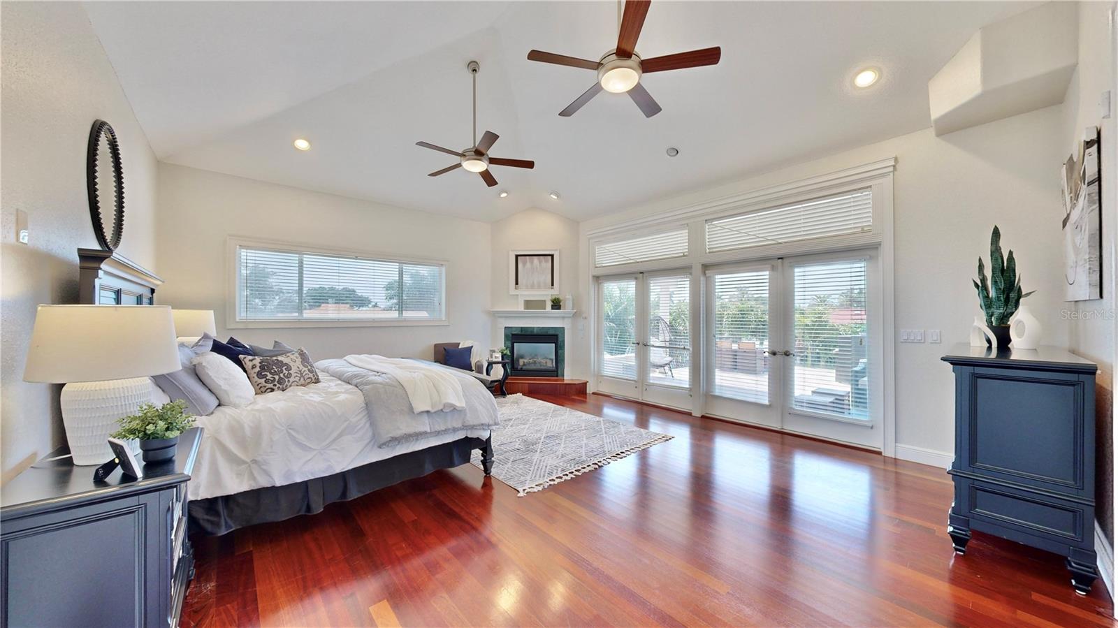 Primary bedroom with double French doors leading to 600 sq ft expansive balcony, vaulted ceiling & dual ceiling fans.