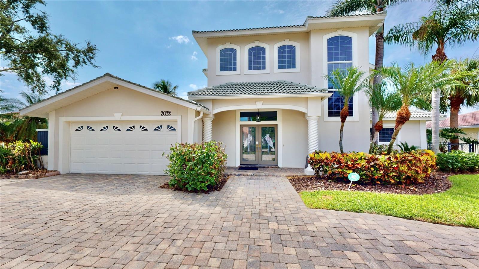 Front of home with U shaped pavered driveway, lush landscaping and gorgeous entryway.