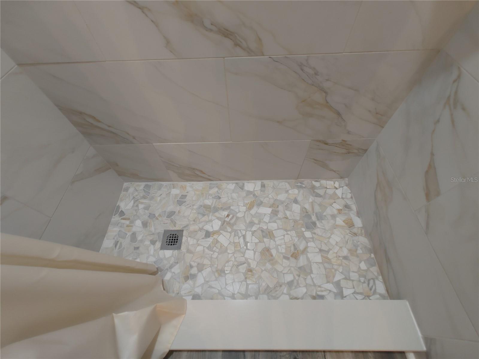 Shower floors and lined with gentle and natural river stone. Shower walls go all the way up to the celing.