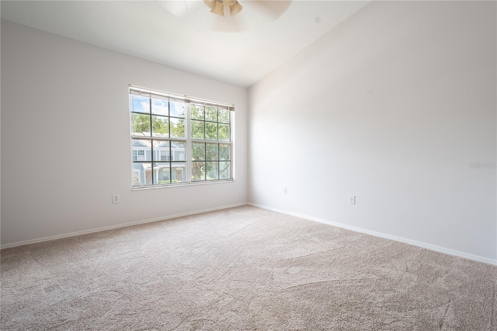 2nd bedroom features a vaulted ceiling, a ceiling fan with light kit, neutral tones, a built-in closet and a large window allowing for natural light.