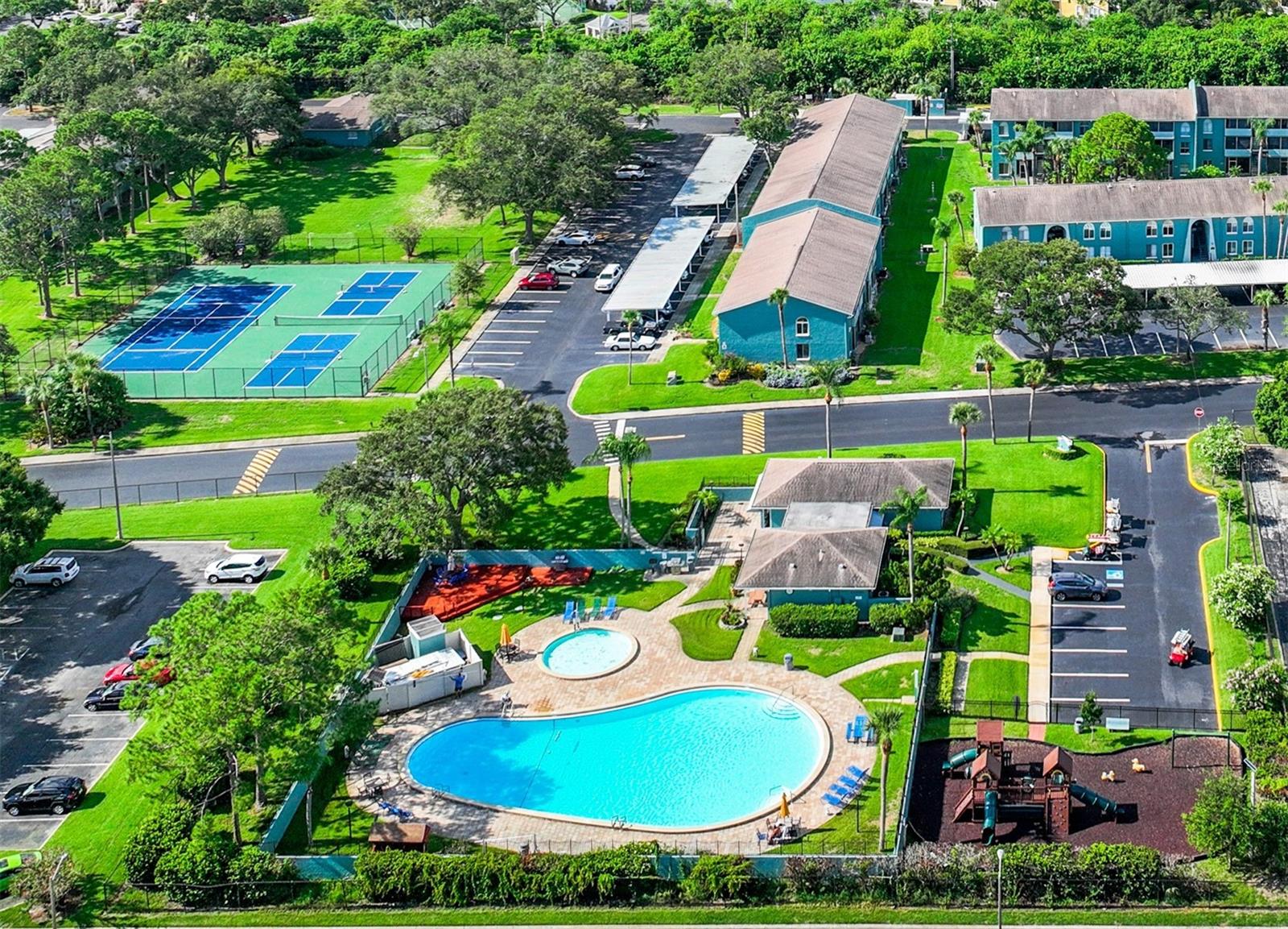 over head of pool, playground, tennis, pickleball, open park. Behind the open park is carwash.