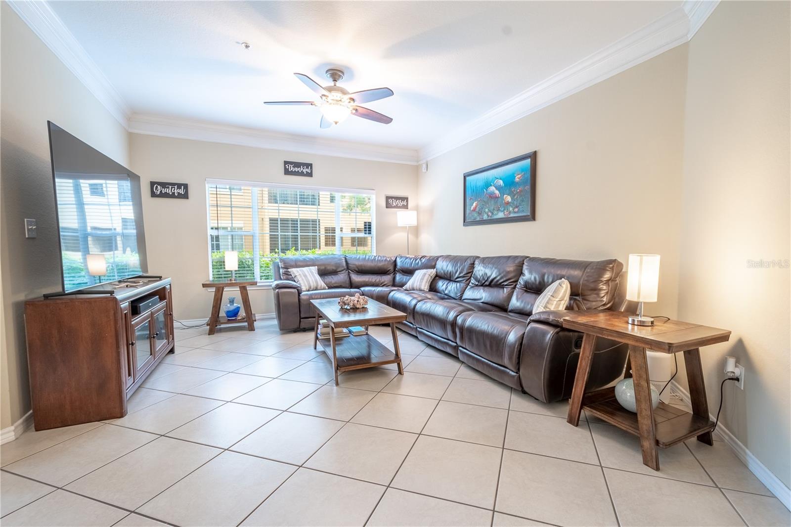 The living room features a ceiling fan with light kit, crown molding, neutral tones and a picture window for plenty of natural light.