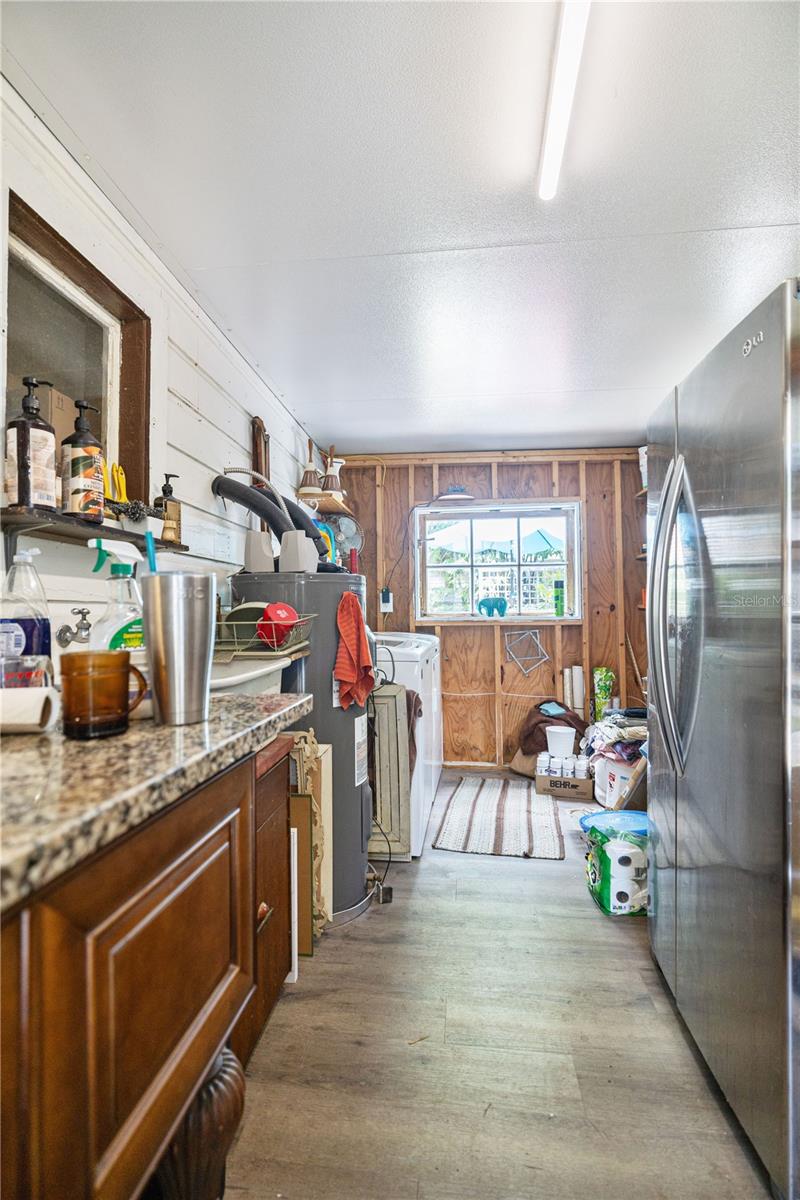 Laundry room with newer water heater, mud sink,  2nd stainless steel side by side Refrigerator and Granite Countertop work table