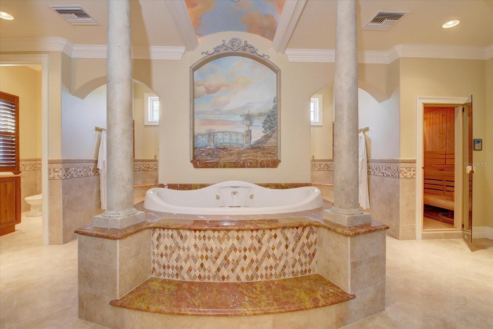 Master Bathroom with enormous, oversized jetted tub with waterfall, aromatherapy, and lighting features, faux painted stone columns with painted mural in niche behind tub