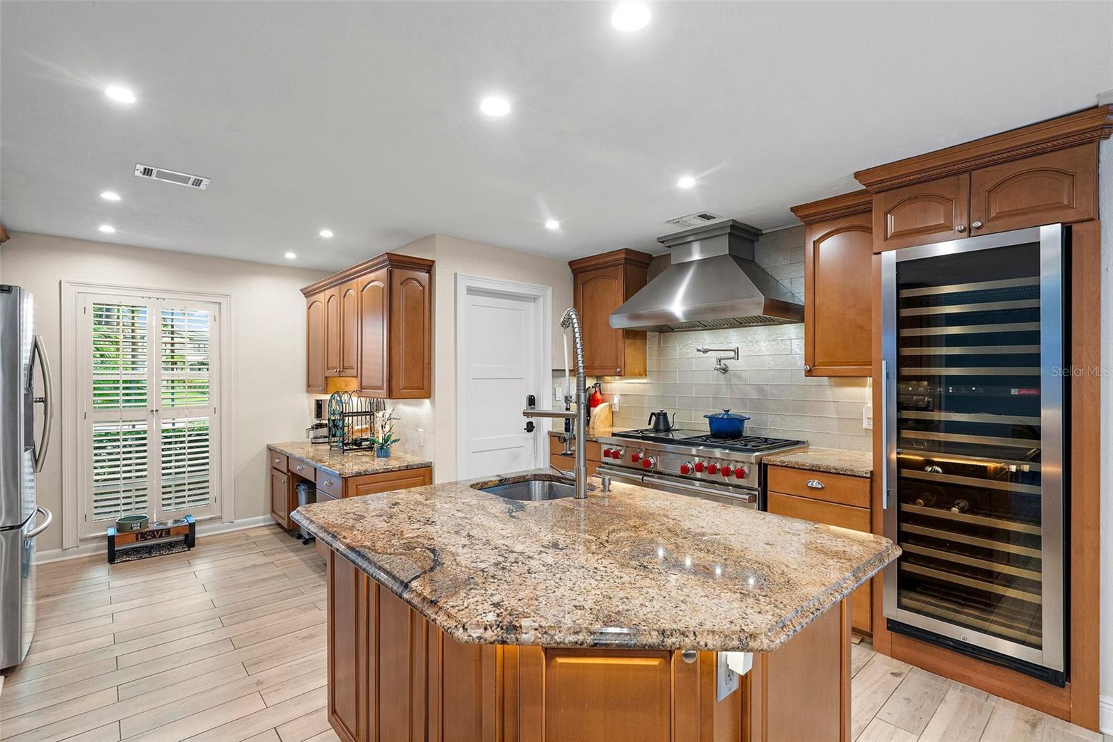 Open kitchen with desk, breakfast nook, island, gas range with pot filler, and wine/beverage cooler