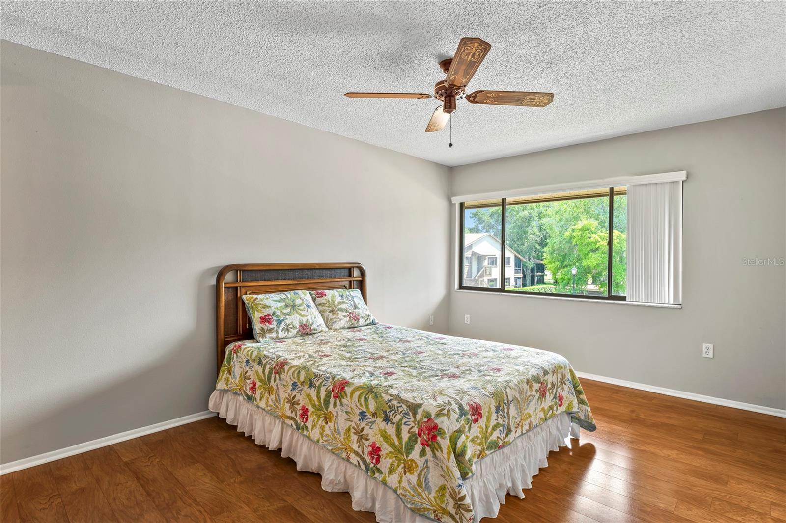 Primary bedroom with ceiling fan, laminated flooring and picture window.