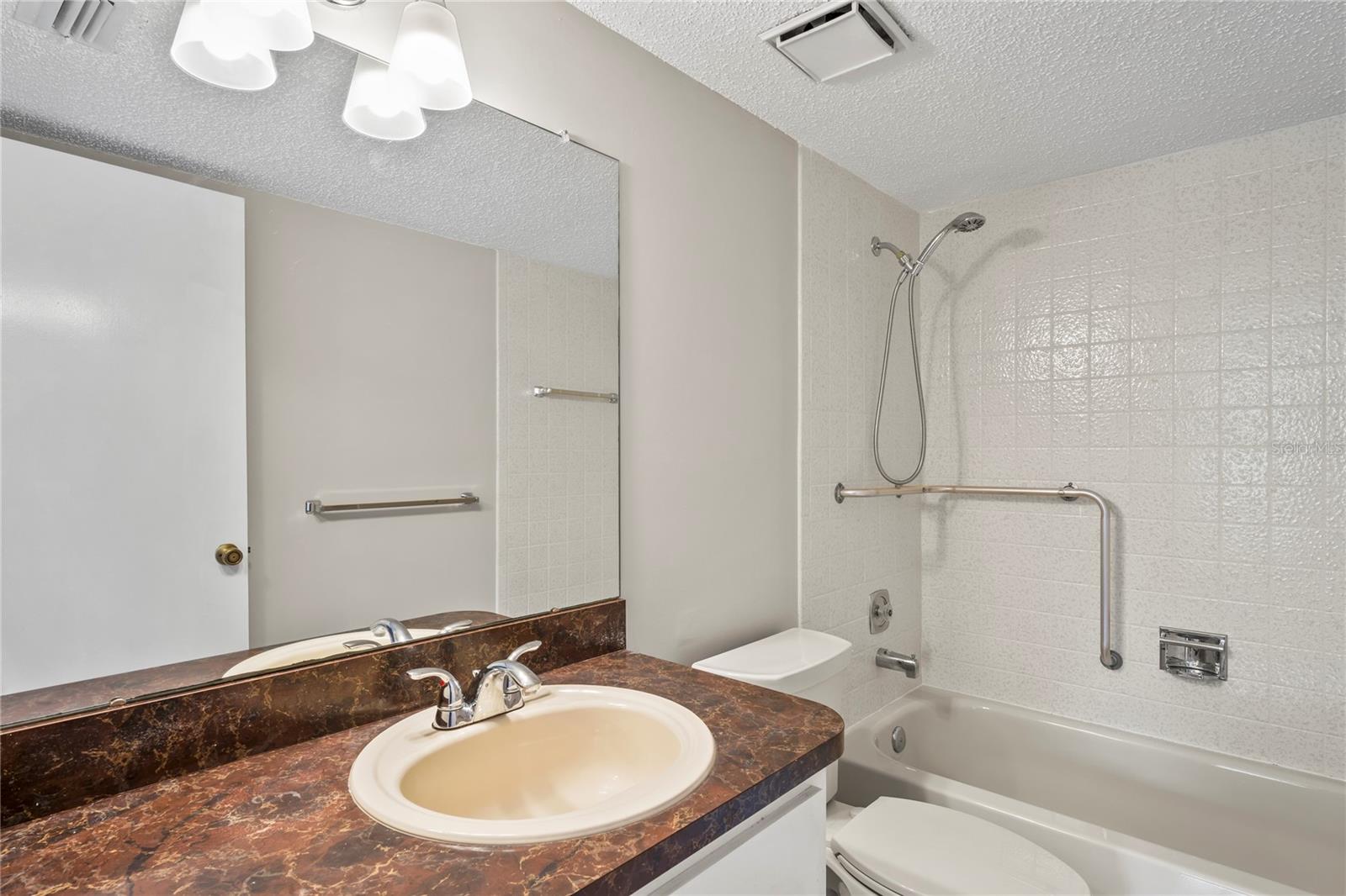 En-suit bathroom has single vanity and tub with a shower including grab bars for safety.