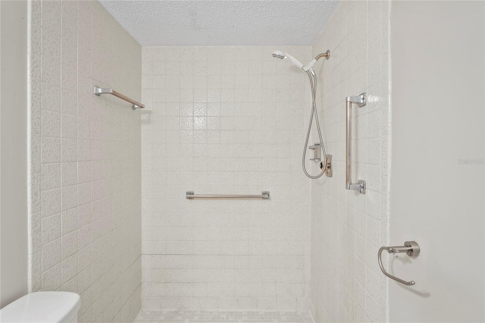 Shower only, no tub, grab bars and ceramic tile on walls and floors.