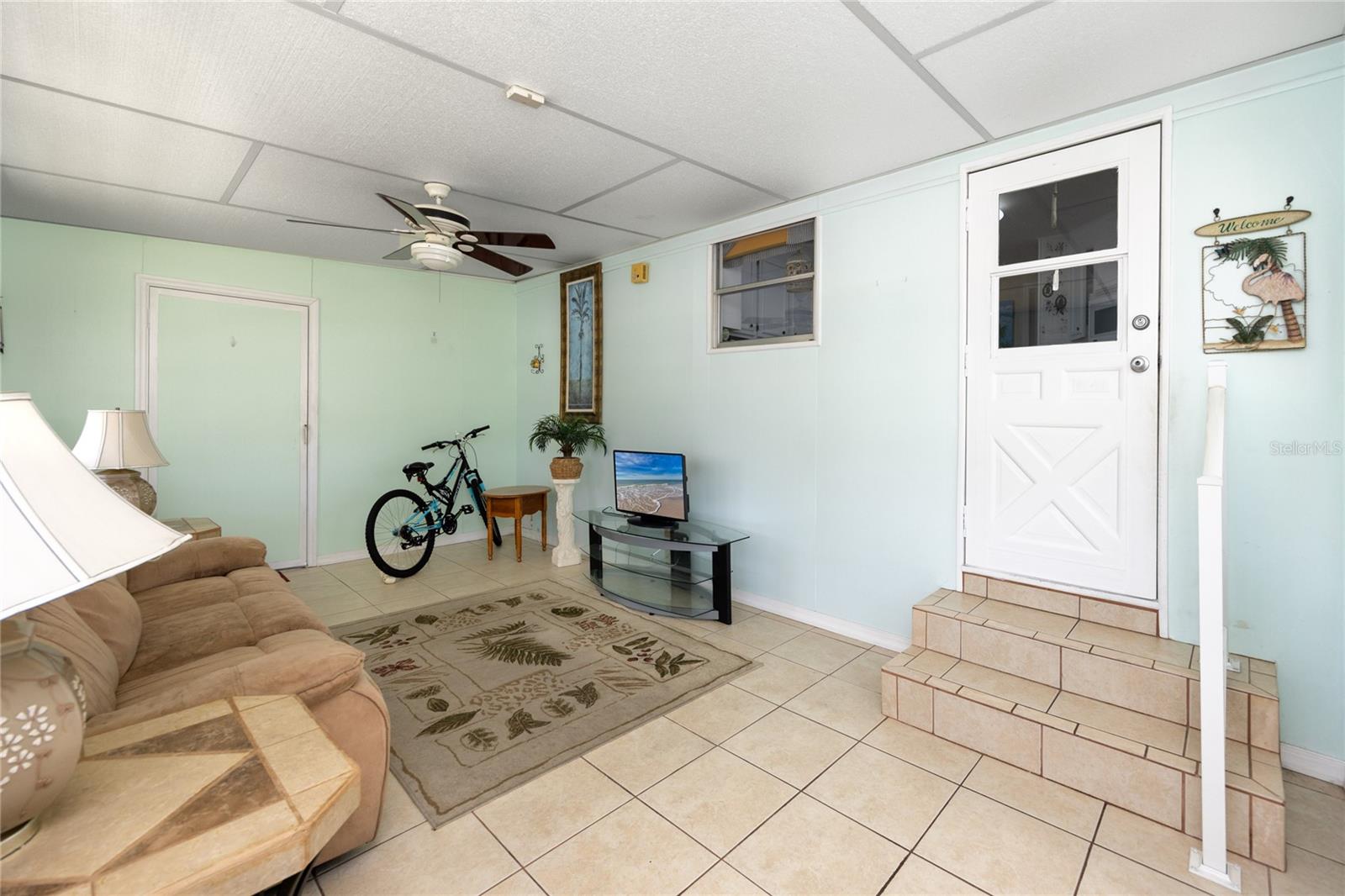 Large enclosed Florida room with direct access from the carport. The green door leads to the laundry room, and the white door leads into the kitchen.