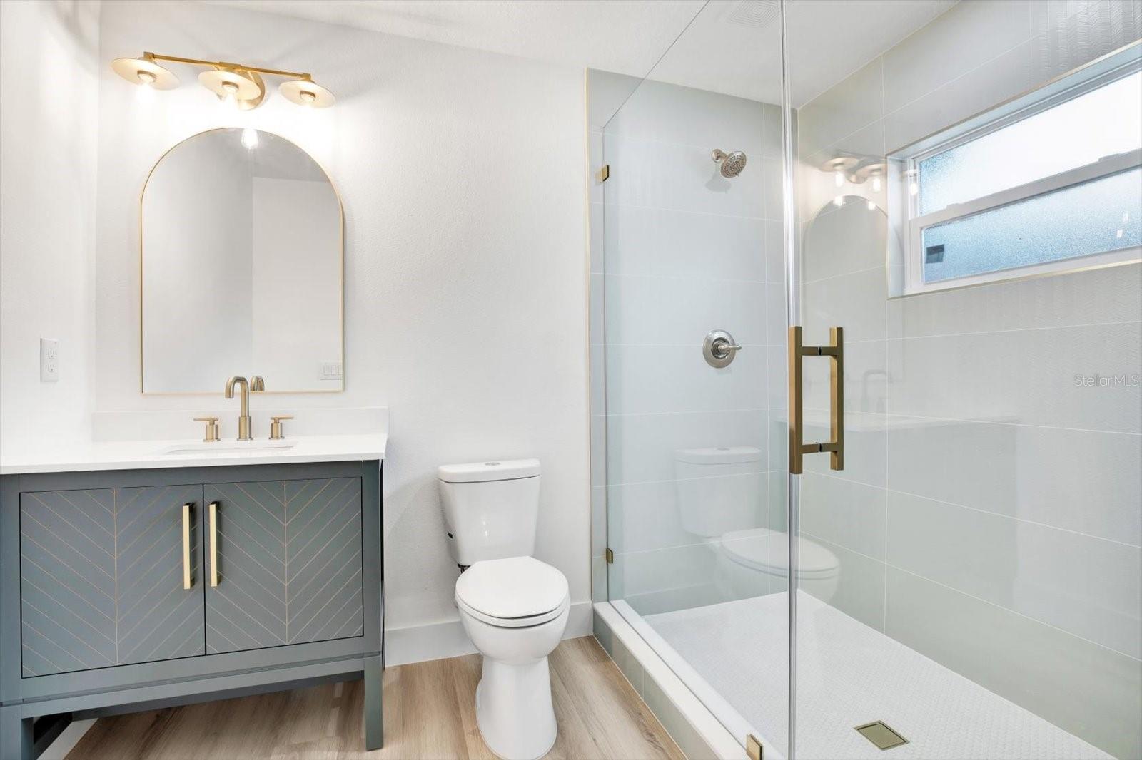 En-suite bathroom of front bedroom with a frameless glass shower that boasts beautiful gold tones and mint green patterned tile