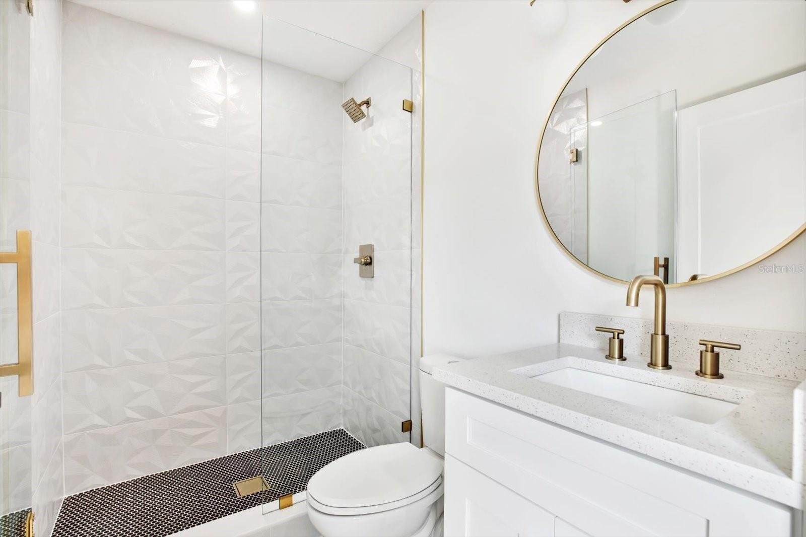 En-suite bathroom of rear bedroom 1 with a frameless glass shower that boasts beautiful gold tones and 3-D geometric tile