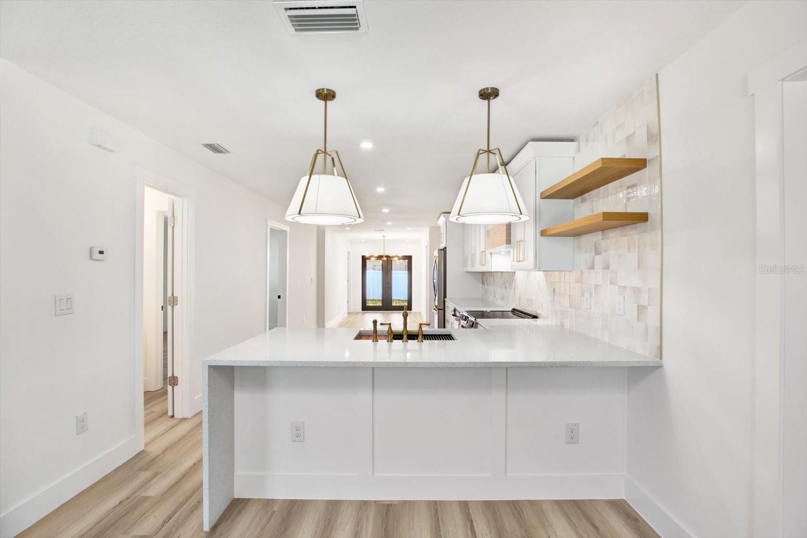 Quartz waterfall kitchen peninsula featuring built-in shelves, pendant lights, and a bridge sink