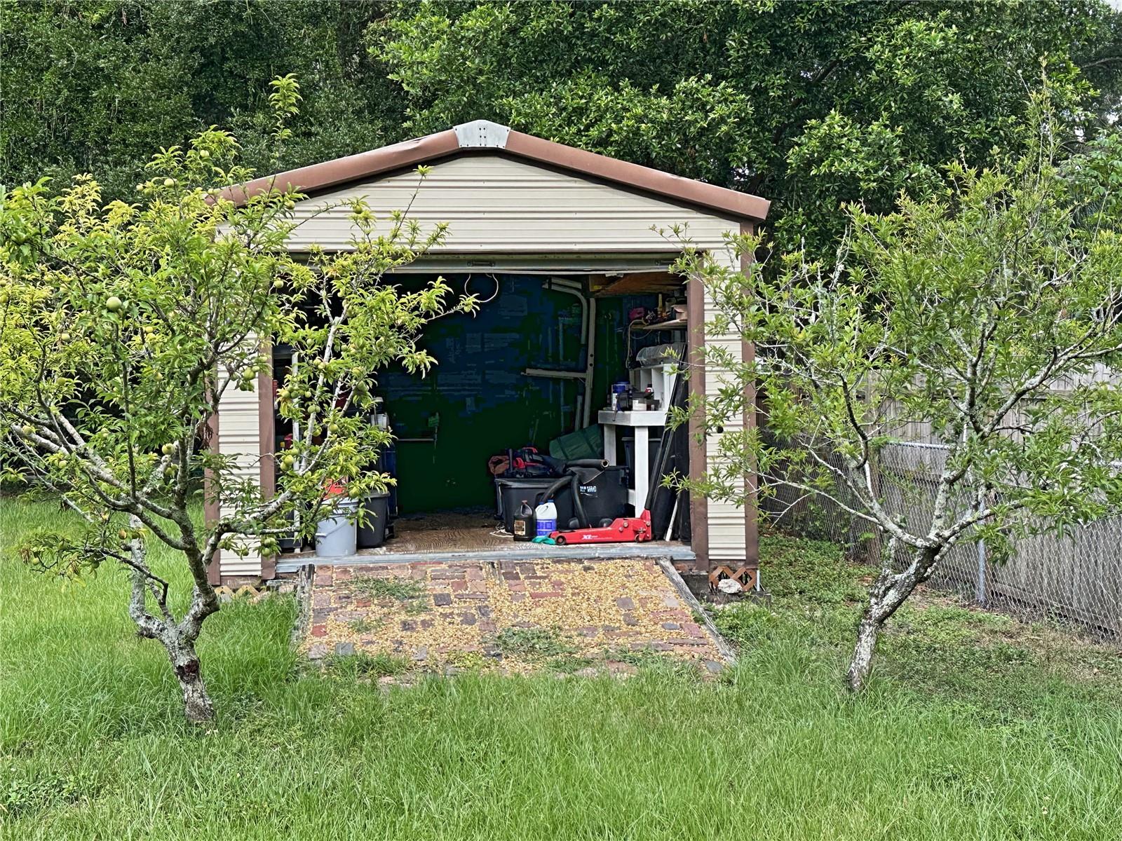 The work shed is 30 feet by 12 feet.  Flanking the shed are two mature plum trees.  There is an entry door as well as an overhead garage door.  The shed is of steel construction and is perfect to use as storage or as a work shop.