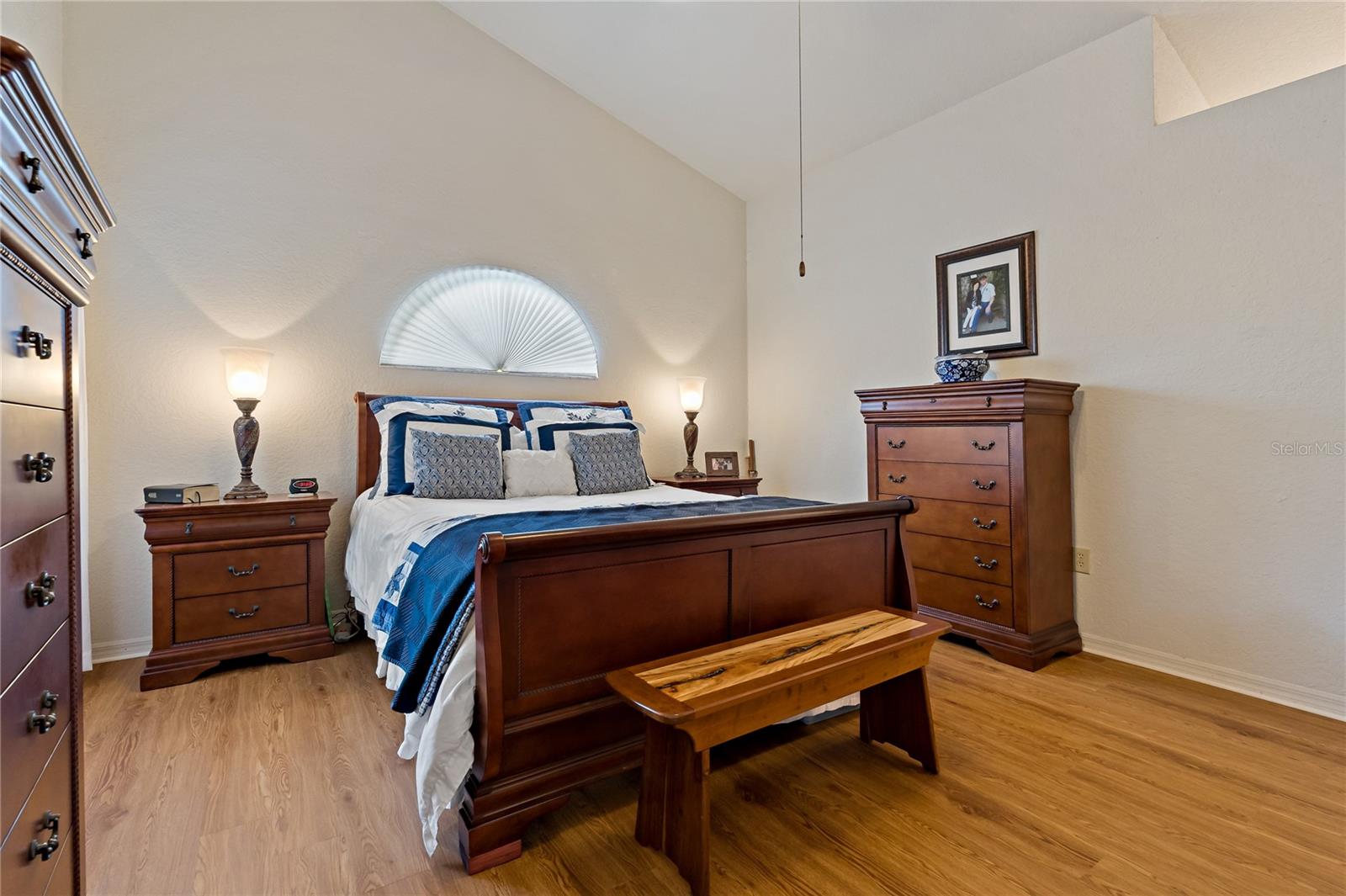 Primary Bedroom With Wood Laminate Flooring and Arched Window over Bed