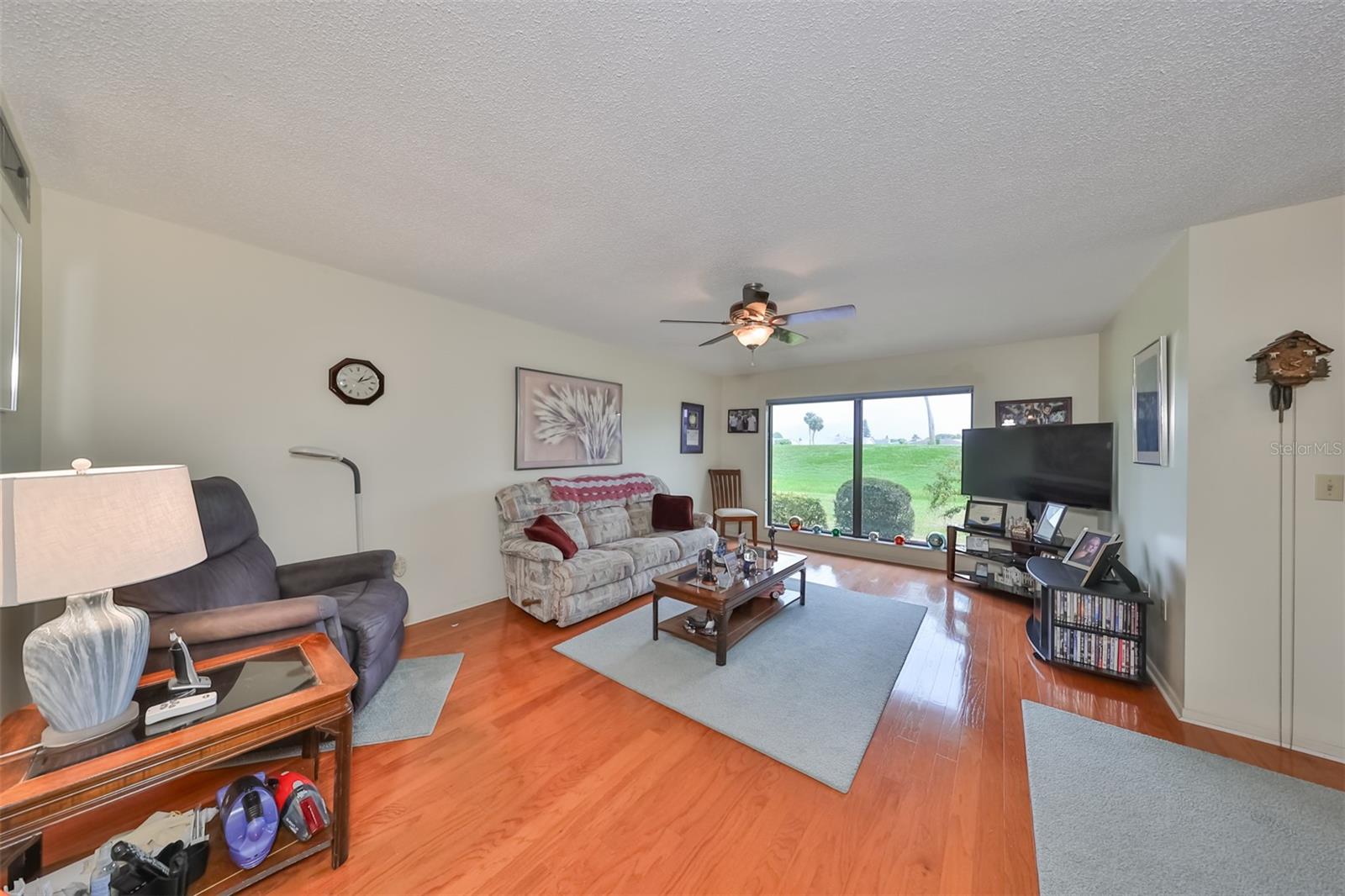 Living room is large with gleaming floors, oversized window panes and ceiling fan.