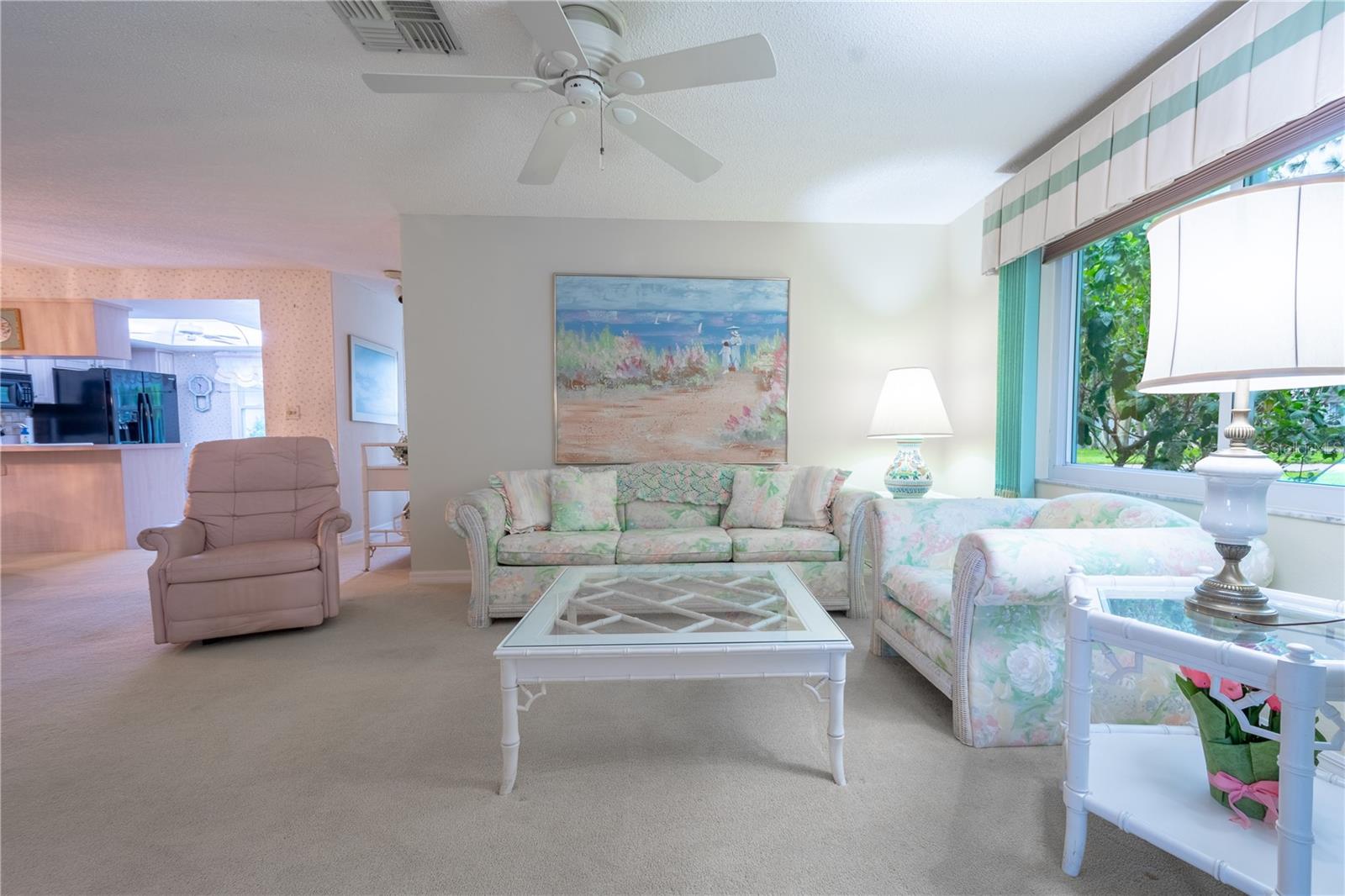 The living room is light and bright with a neutral color palette, plush carpet and a ceiling fan with light kit.