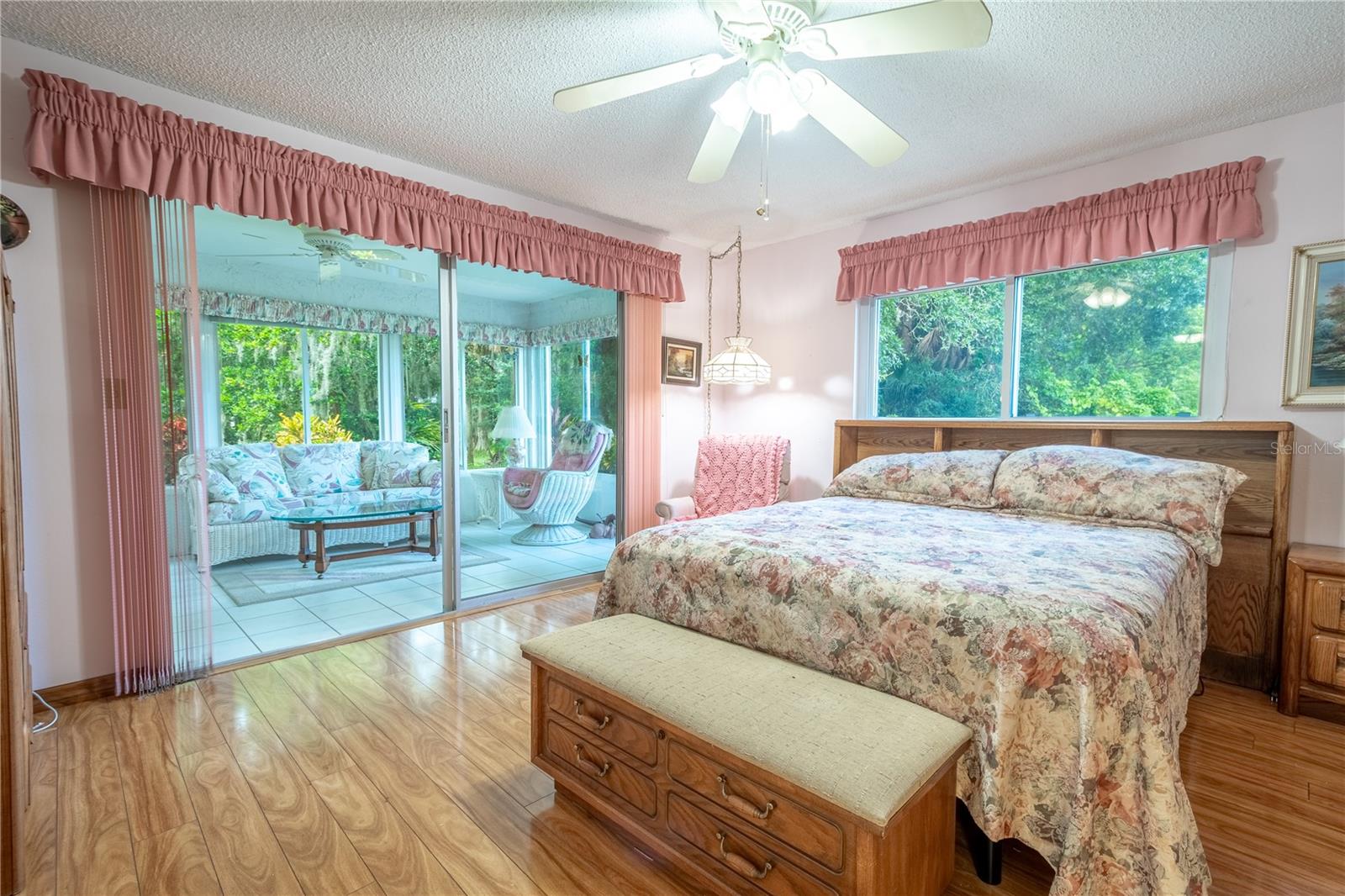 The primary bedroom features neutral tones, a wood laminate floor, a ceiling fan with light kit and sliding glass doors that open to the Florida Room.