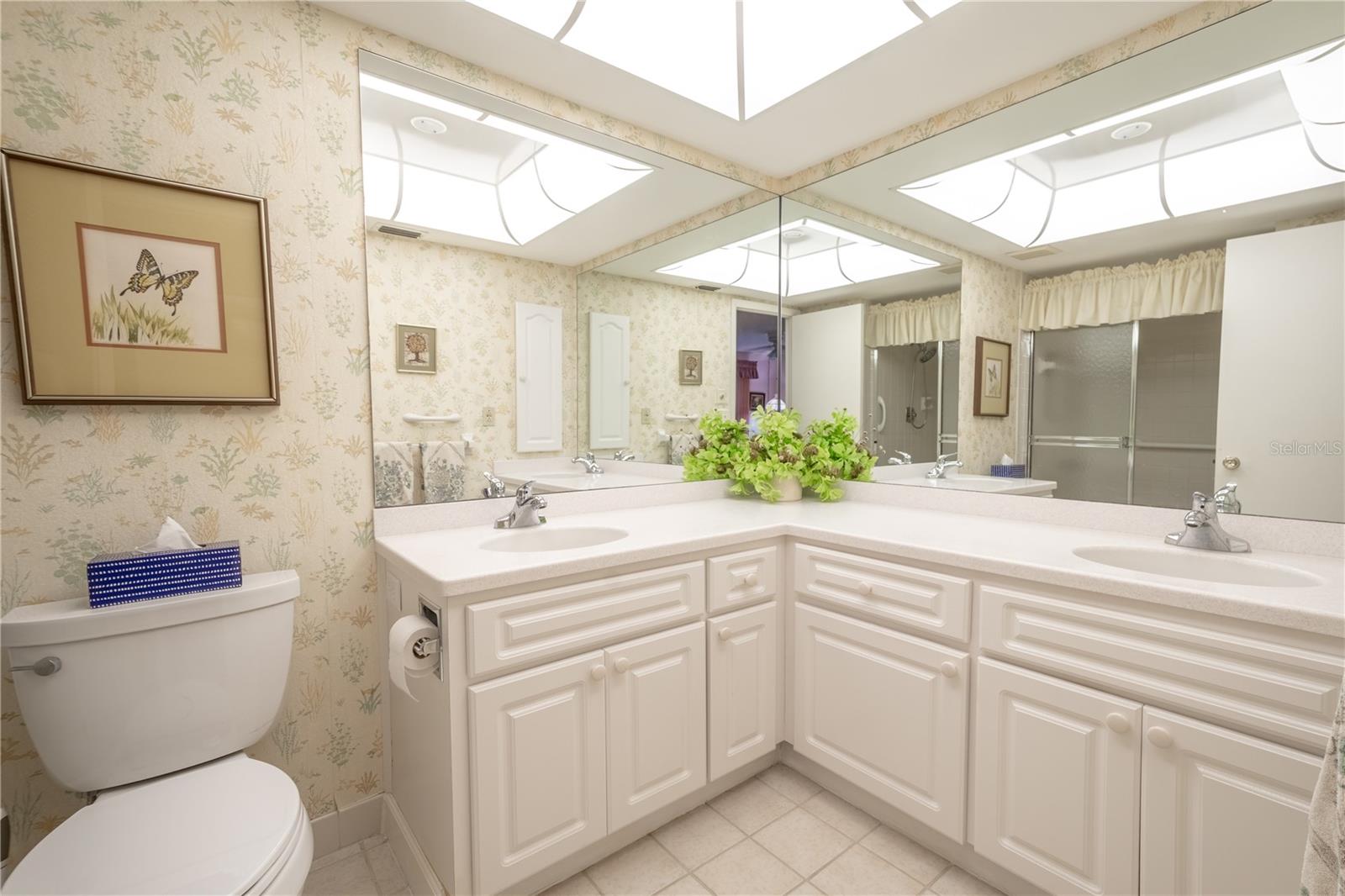 The primary bath features a dual sink mirrored vanity with refaced cabinets and corian countertop, a lighted dome ceiling and a ceramic tile floor.