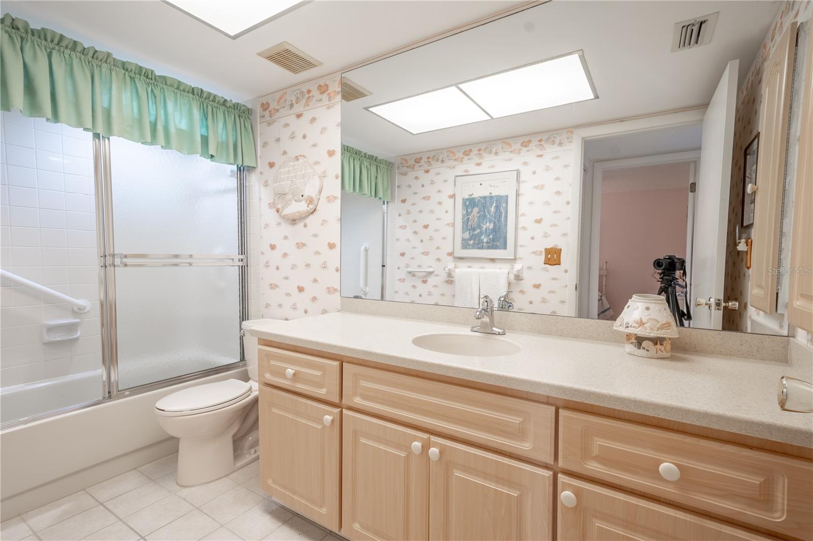 Bathroom Two features a ceramic tile floor, a tub with shower, and a mirrored vanity with refaced cabinets and corian countertop.