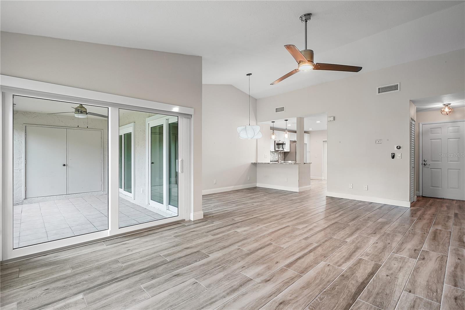 Unfurnished living room showing the attached patio with storage beyond the double doors, the living room/dining room combo, the breakfast bar leading into the kitchen.