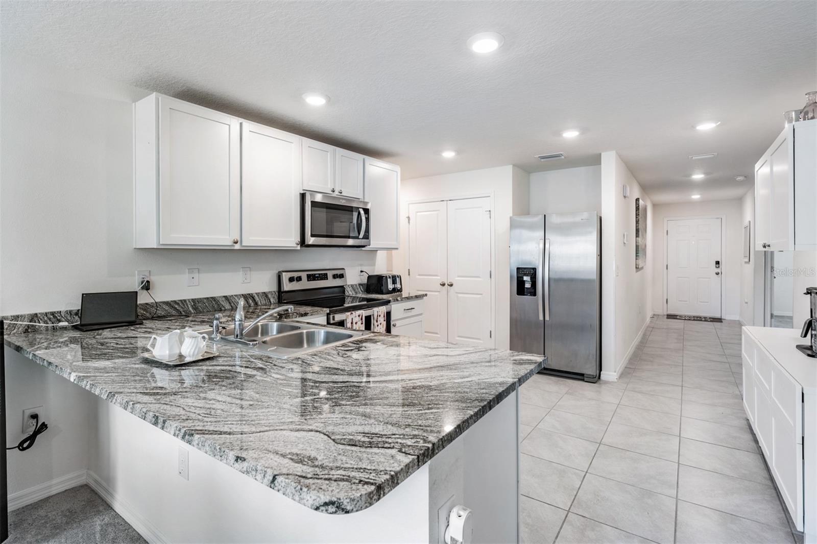 Large and open kitchen with tile flooring, inset lighting, double door pantry and stainless steel applian