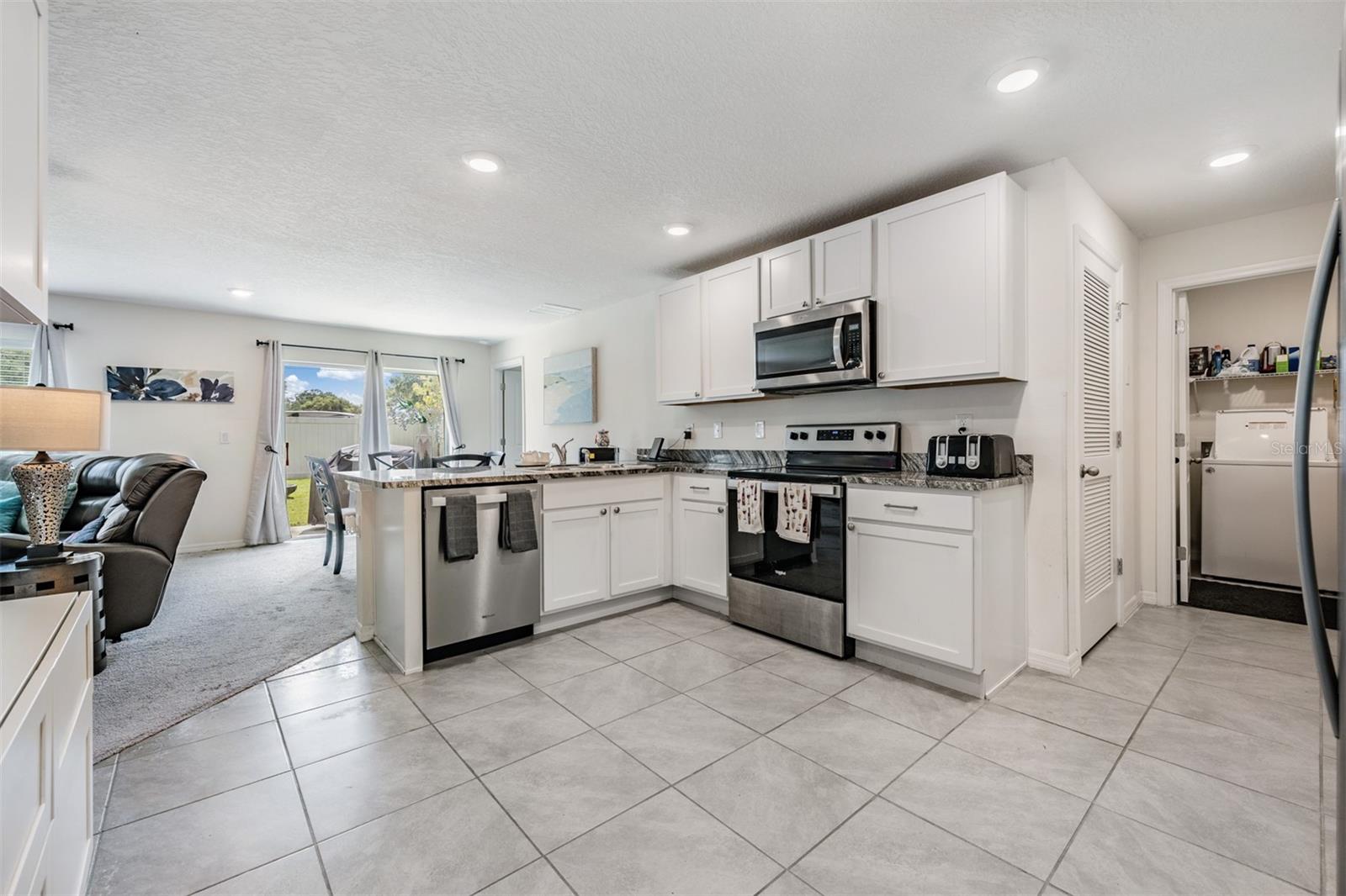 Large and open kitchen with tile flooring, inset lighting, double door pantry and stainless steel appliances