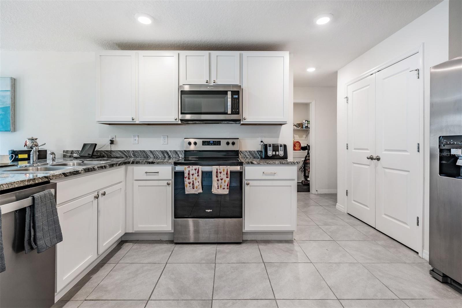 Large and open kitchen with tile flooring, inset lighting, double door pantry and stainless steel appliances