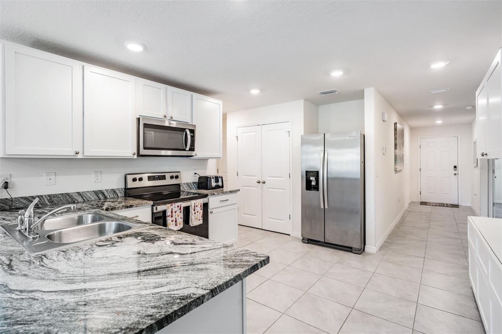 Large and open kitchen with tile flooring, inset lighting, double door pantry and stainless steel appliances