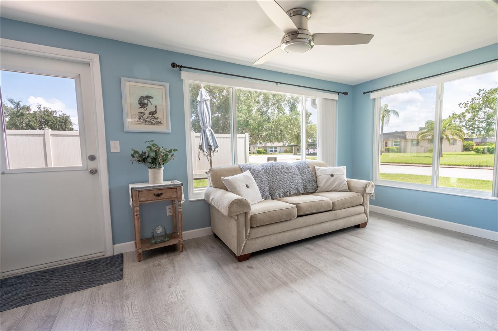 The Florida room showcases neutral-toned wood laminate flooring, a ceiling fan, and impact-resistant windows installed in 2022.