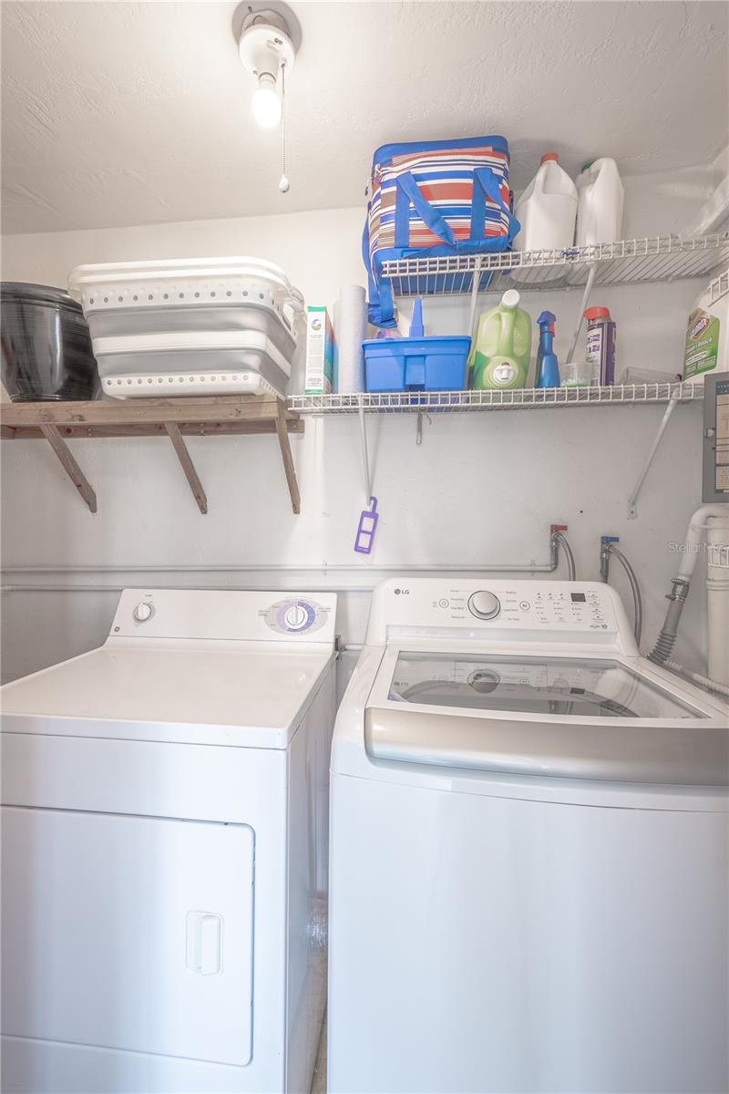 Located in the Florida room, there is a large laundry closet with a washer, dryer and shelving above.