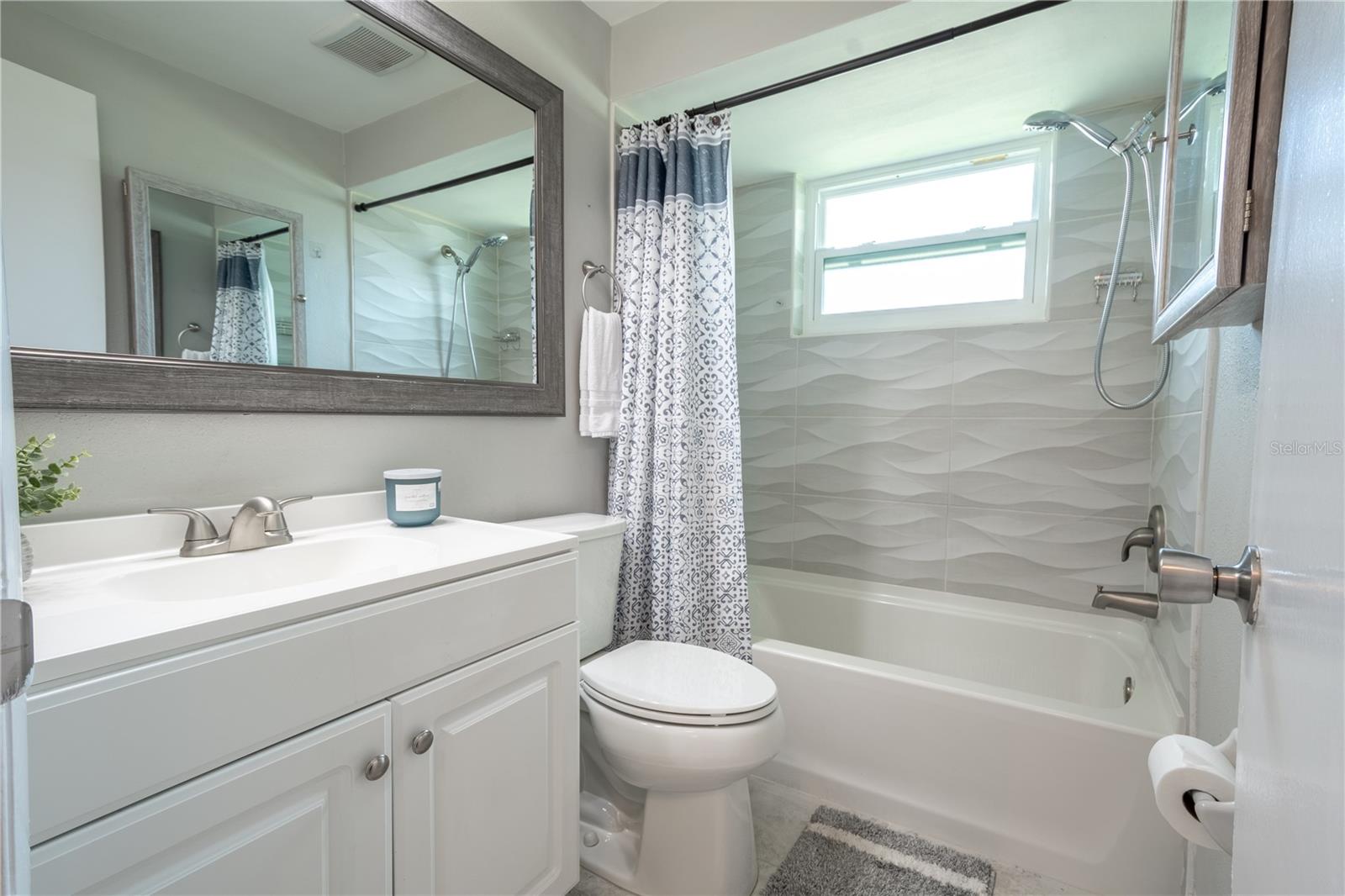 Bathroom 2 features an artistic tiled tub with shower, and a mirrored vanity with storage.