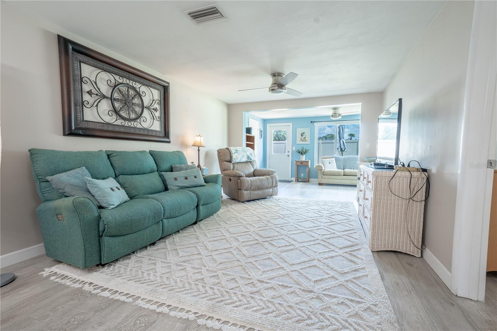 The living room is light and bright bather in a natural color palette, with wood laminate flooring and a ceiling fan.