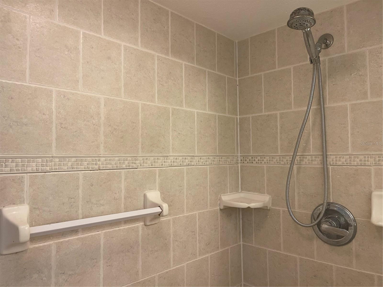 Shower in primary bathroom has wall to wall ceramic tiles.