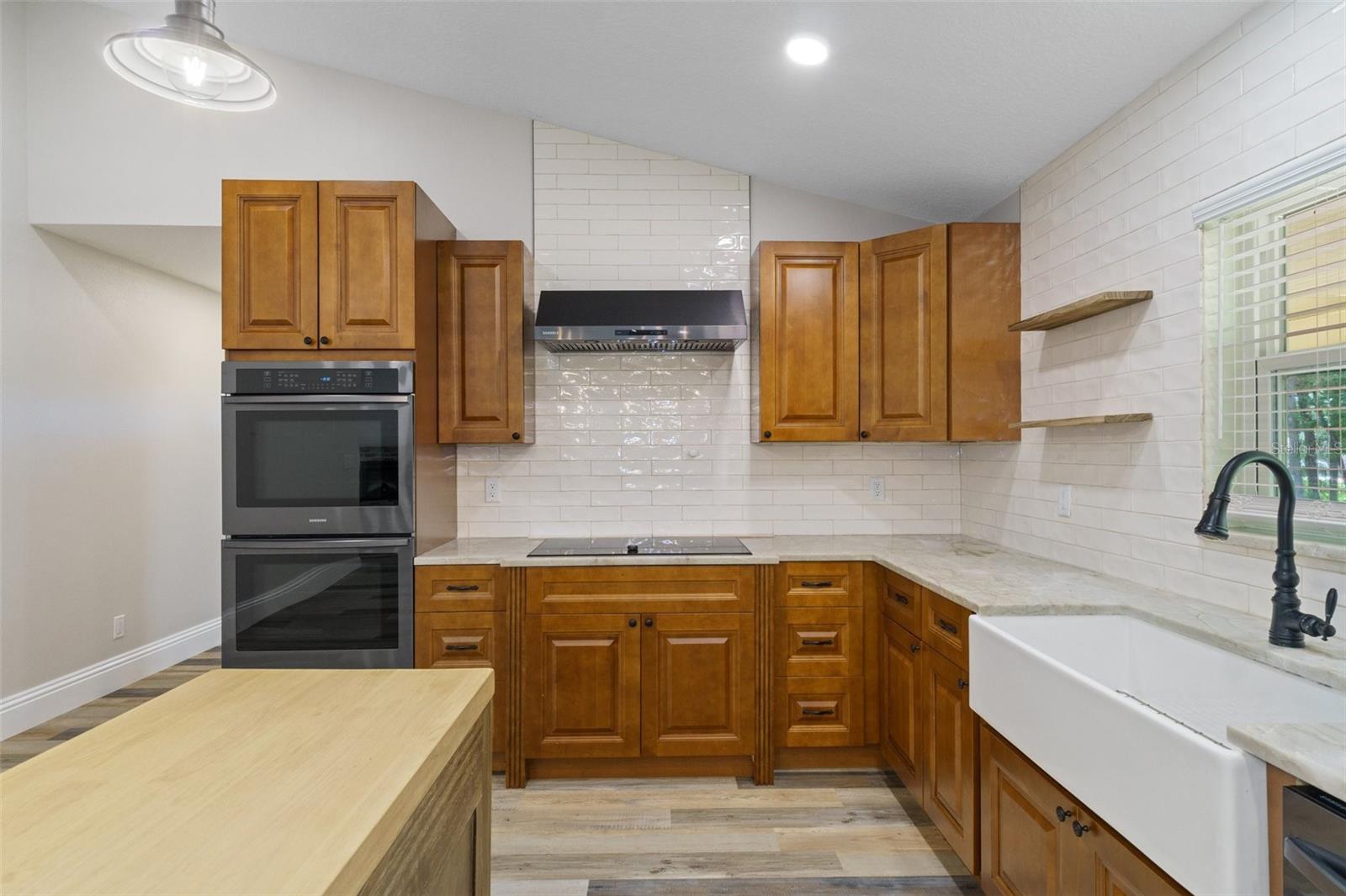 Kitchen features farm sink, Samsung stainless appliances, stone counter and white subway tiles.