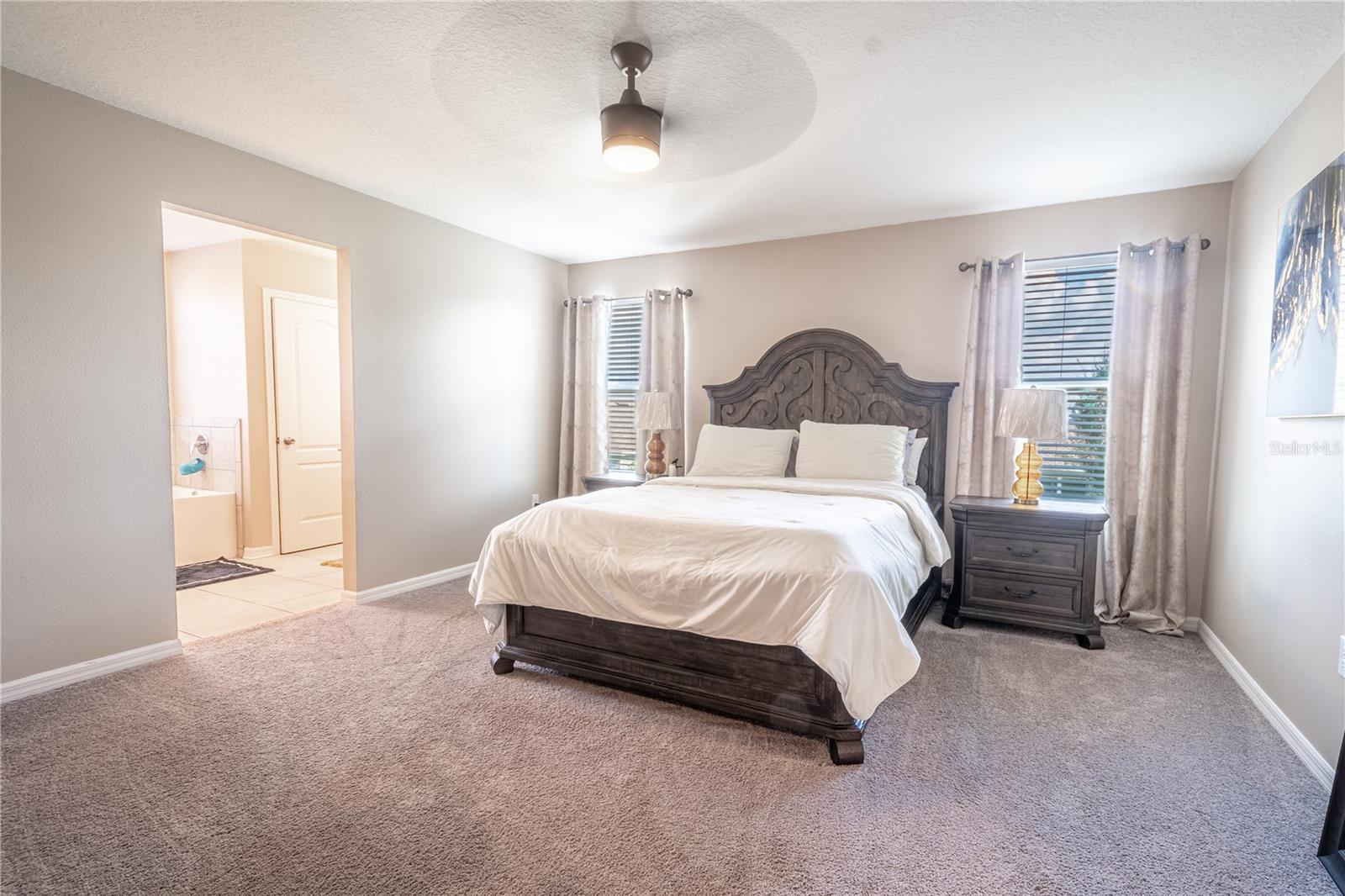 The primary bedroom features plush neutral toned carpet, 8' ceilings, a ceiling fan, a walk-in closet and ensuite bath.