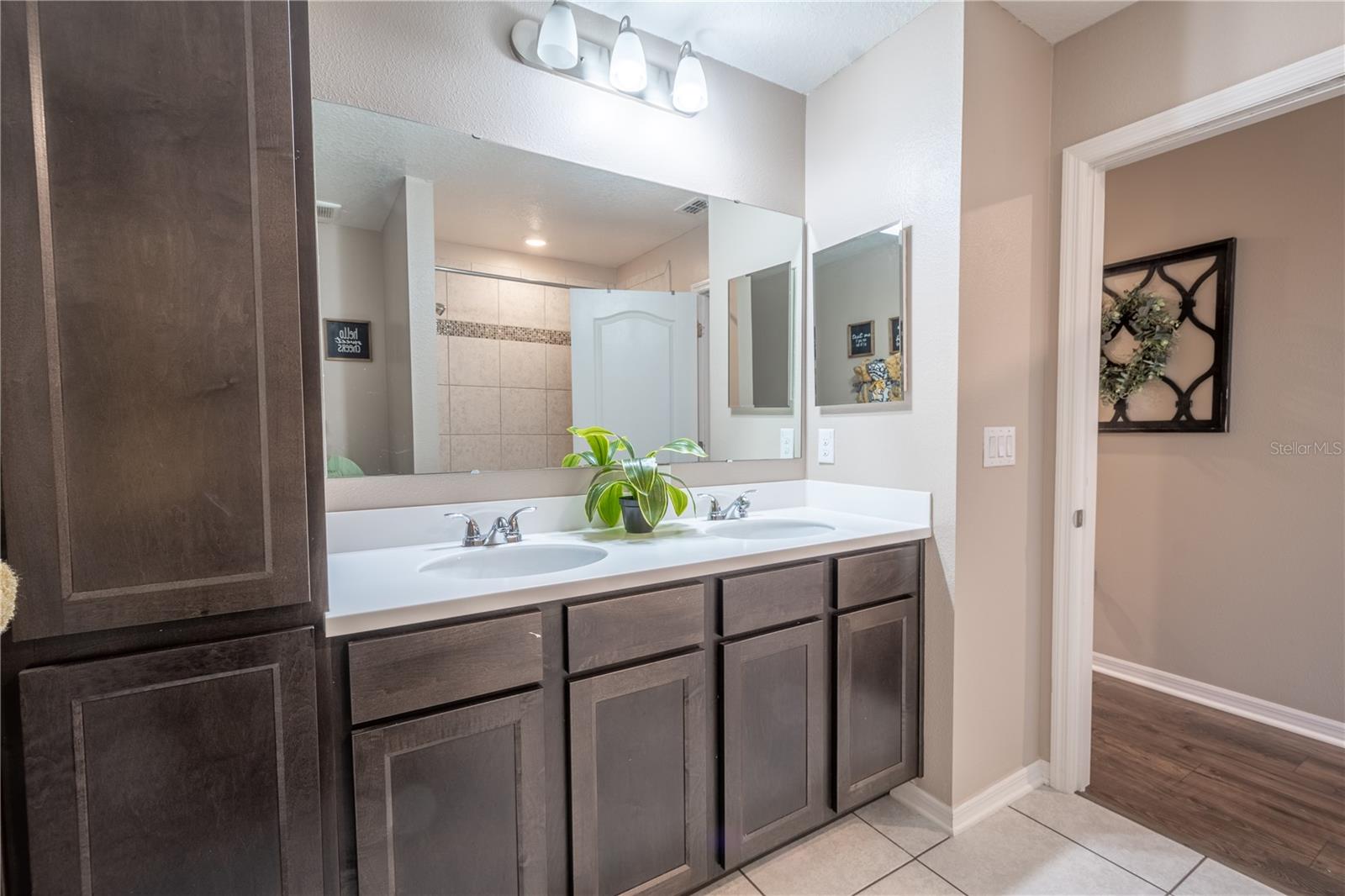 Bathroom Three features a mirrored, dual sink wood vanity with storage and downlight fixture, a tub with shower and ceramic tile flooring.