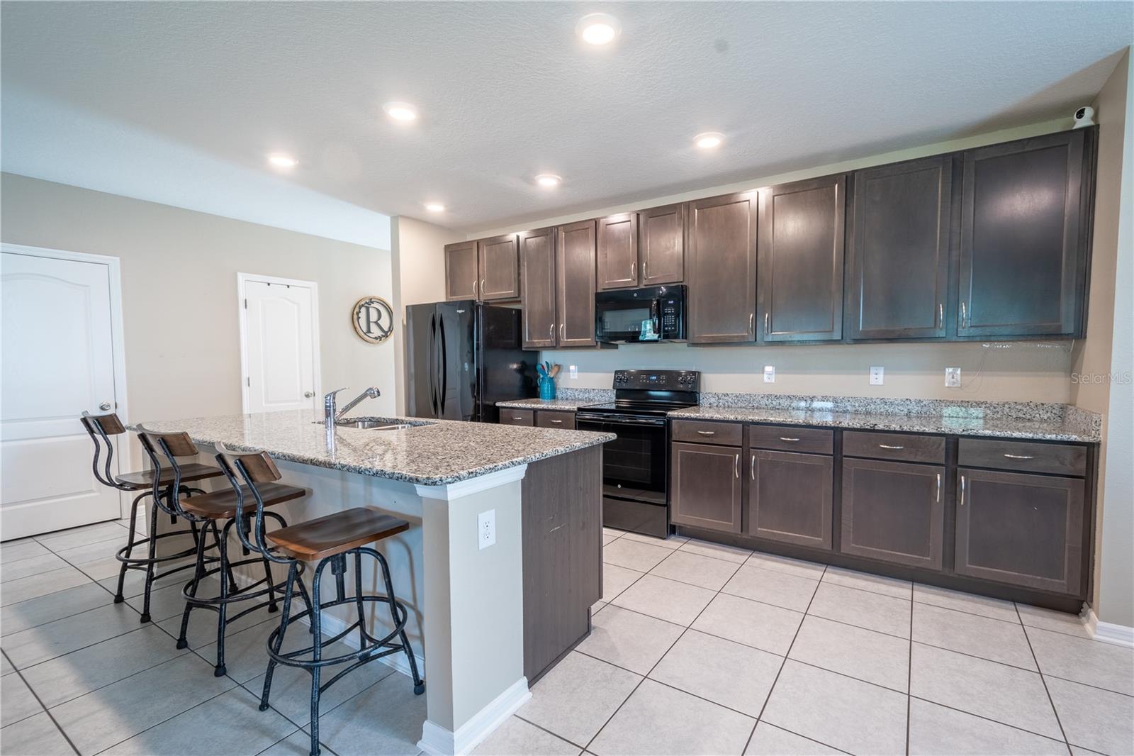 The kitchen features rich chocolate wood cabinets, ceramic tile flooring, granite countertops, recessed lighting, and a full suite of GE appliances.