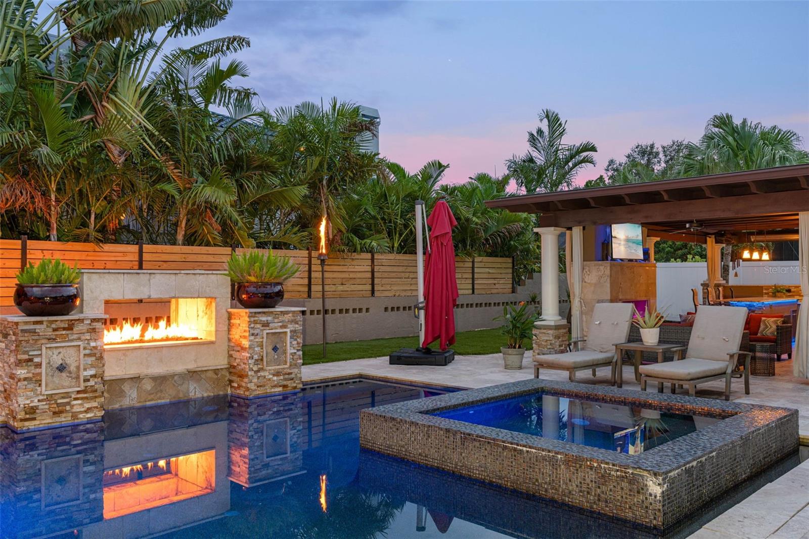 This listing features a tropical oasis with an outdoor fireplace and a sparkling pool, creating a serene and inviting atmosphere.