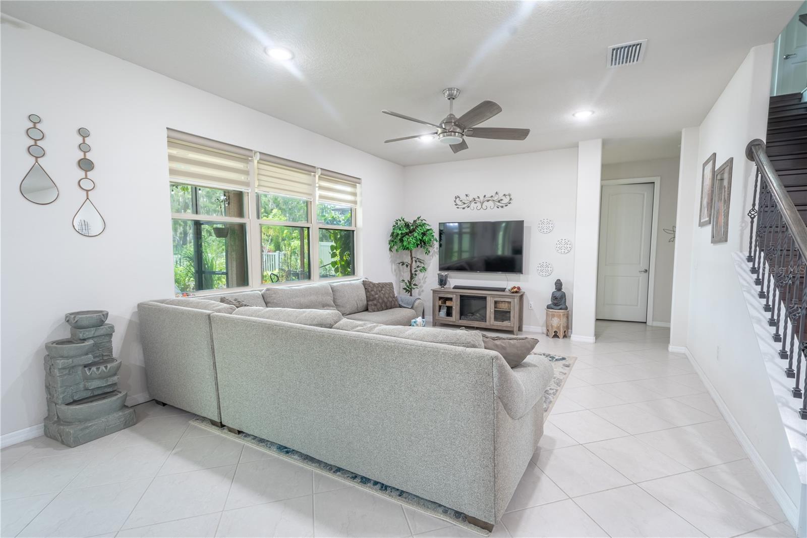 The family room features neutral tones, a ceiling fan with light kit, ceramic tile flooring and plenty of natural light through the trio of windows framing the backyard.