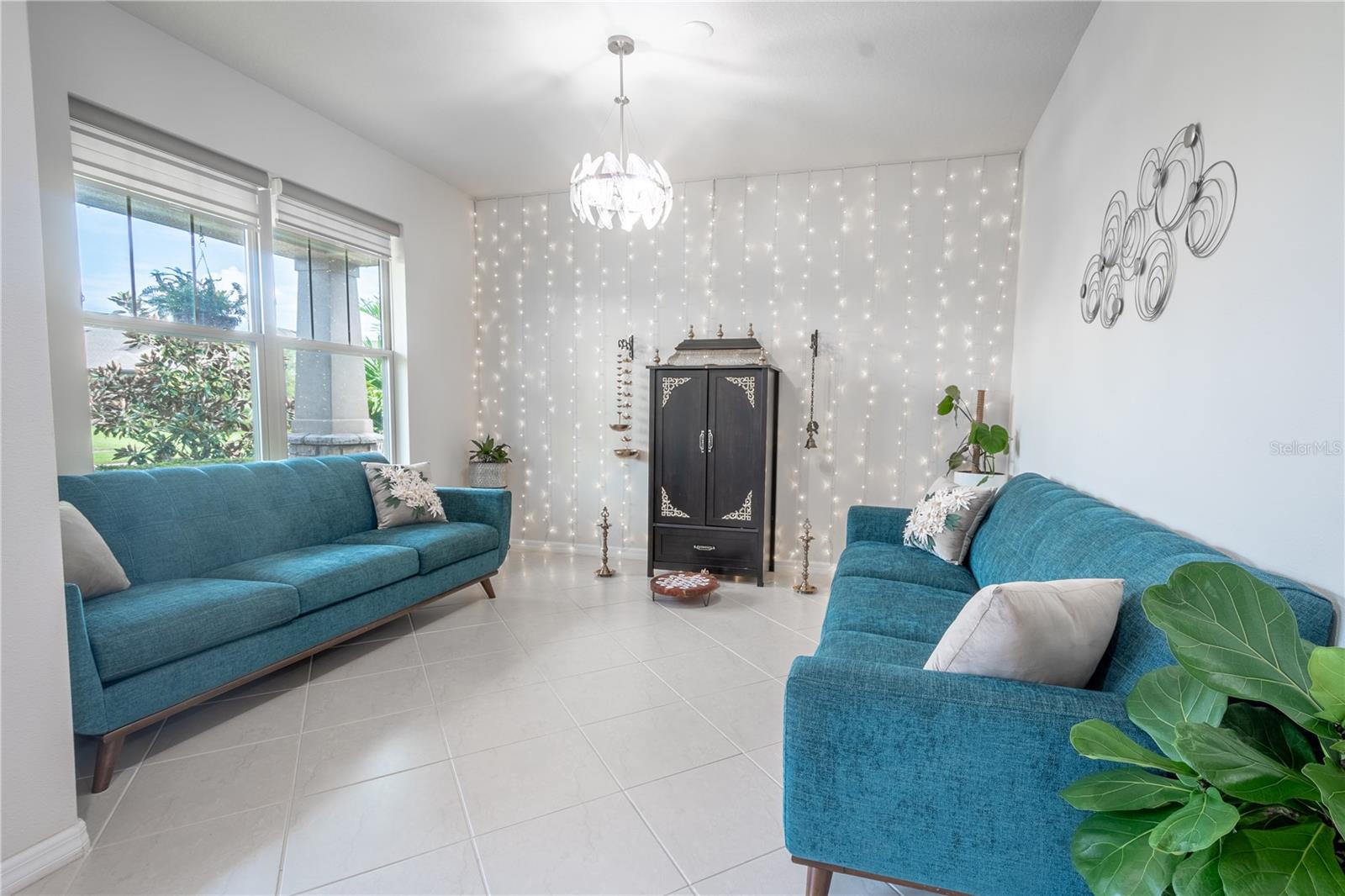 Light and bright living room bathed in natural light with ceramic tile floor, picture window and a chandelier.