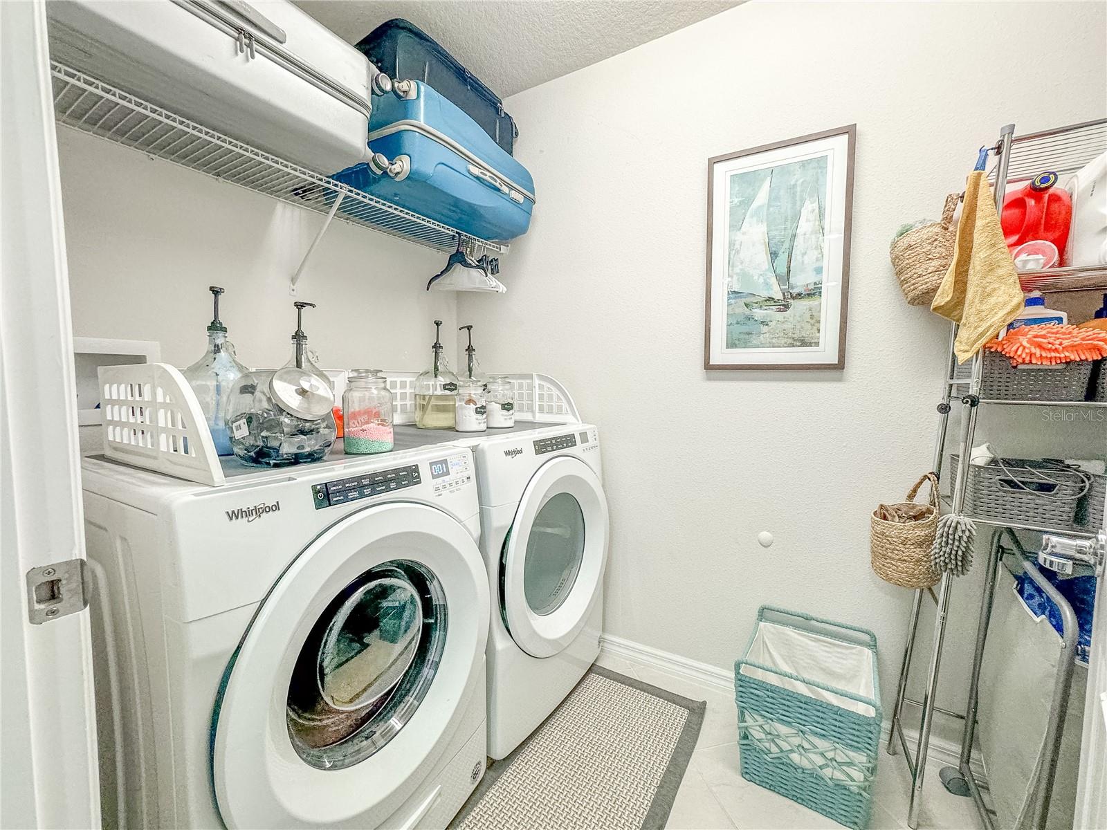 The upstairs laundry room features Whirlpool Washer and dryer (2019), ceramic tile floor and overhead shelving.